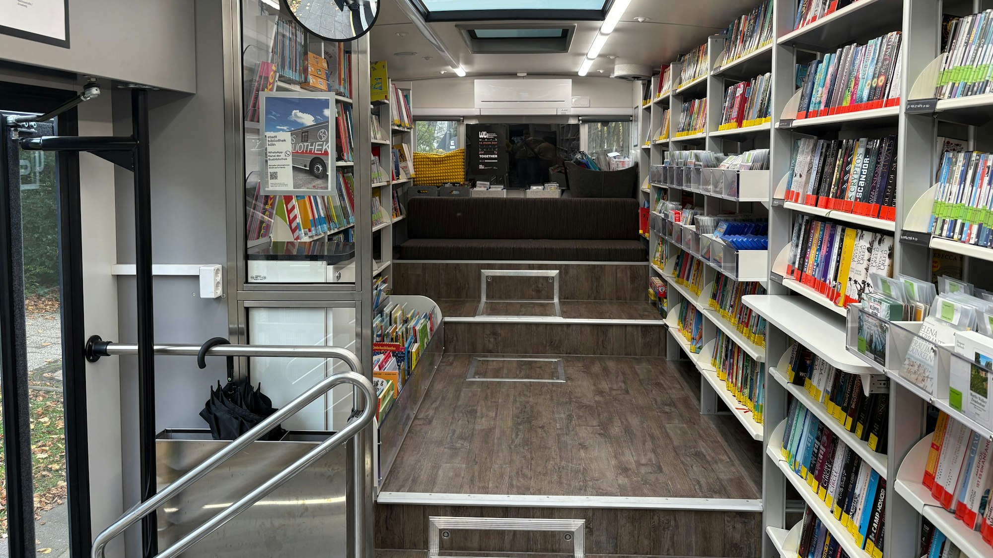 Die Inneneinrichtung der Busbibliothek: An den Seiten sind weiße Regale mit Büchern gefüllt, in der Mitte ein geräumiger Flur. Am Ende des Flurs ist eine Sitzgelegenheit.