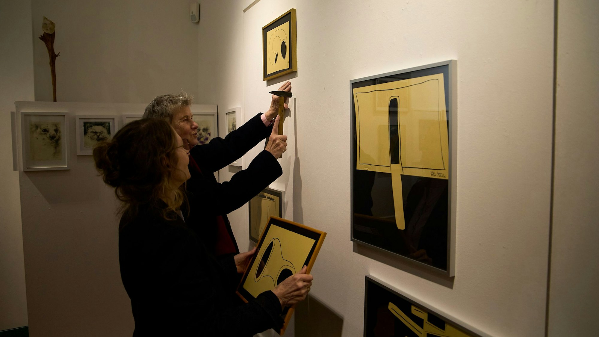 Eine Künstlerin hat einen Hammer in der Hand, die andere hält ein Bild.