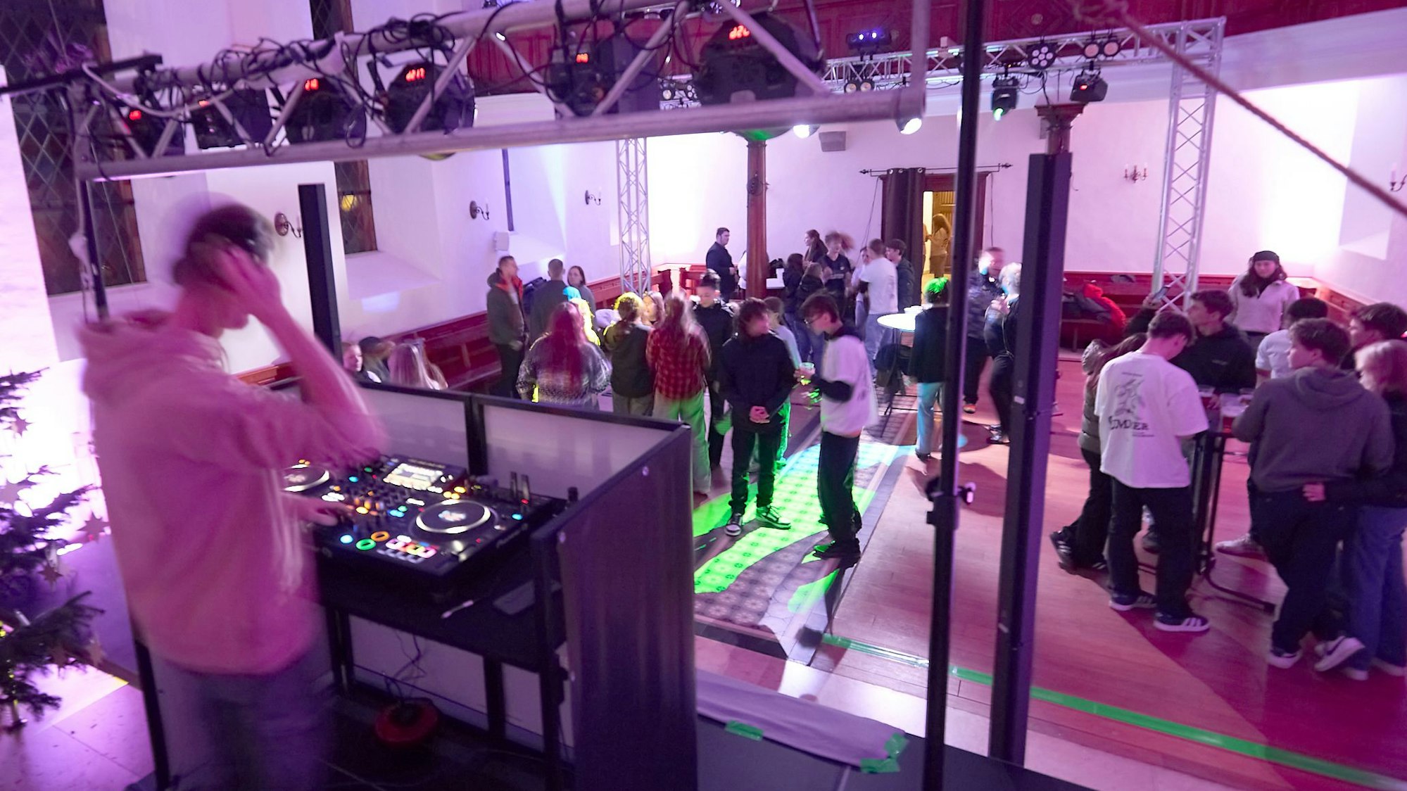 Der Kircheninnenraum ist bunt beleuchtet, etliche junge Menschen tanzen oder stehen an Biertischen zusammen. Im Vordergrund sieht man den DJ an seinem Pult.