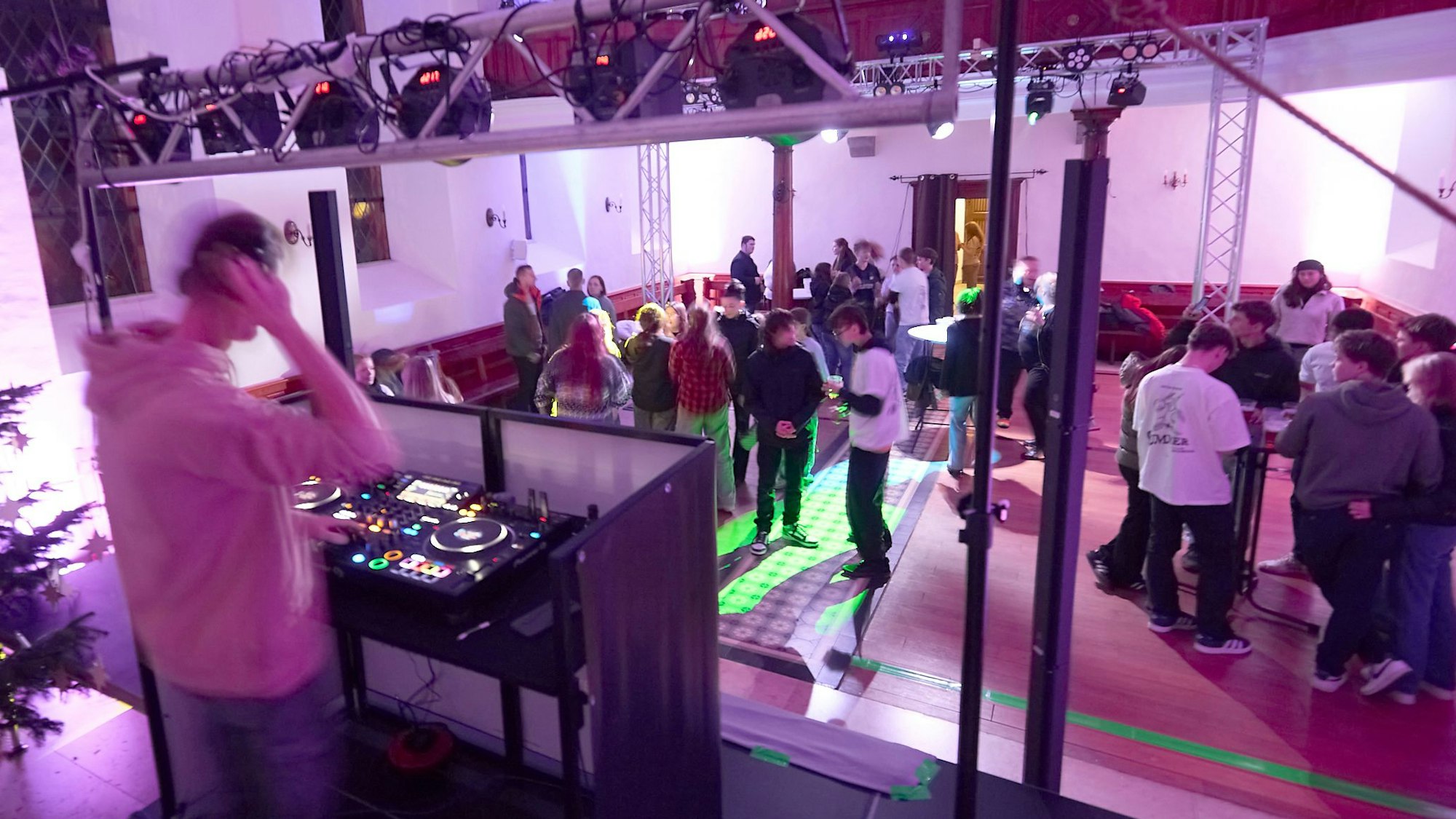 Der Kircheninnenraum ist bunt beleuchtet, etliche junge Menschen tanzen oder stehen an Biertischen zusammen. Im Vordergrund sieht man den DJ an seinem Pult.