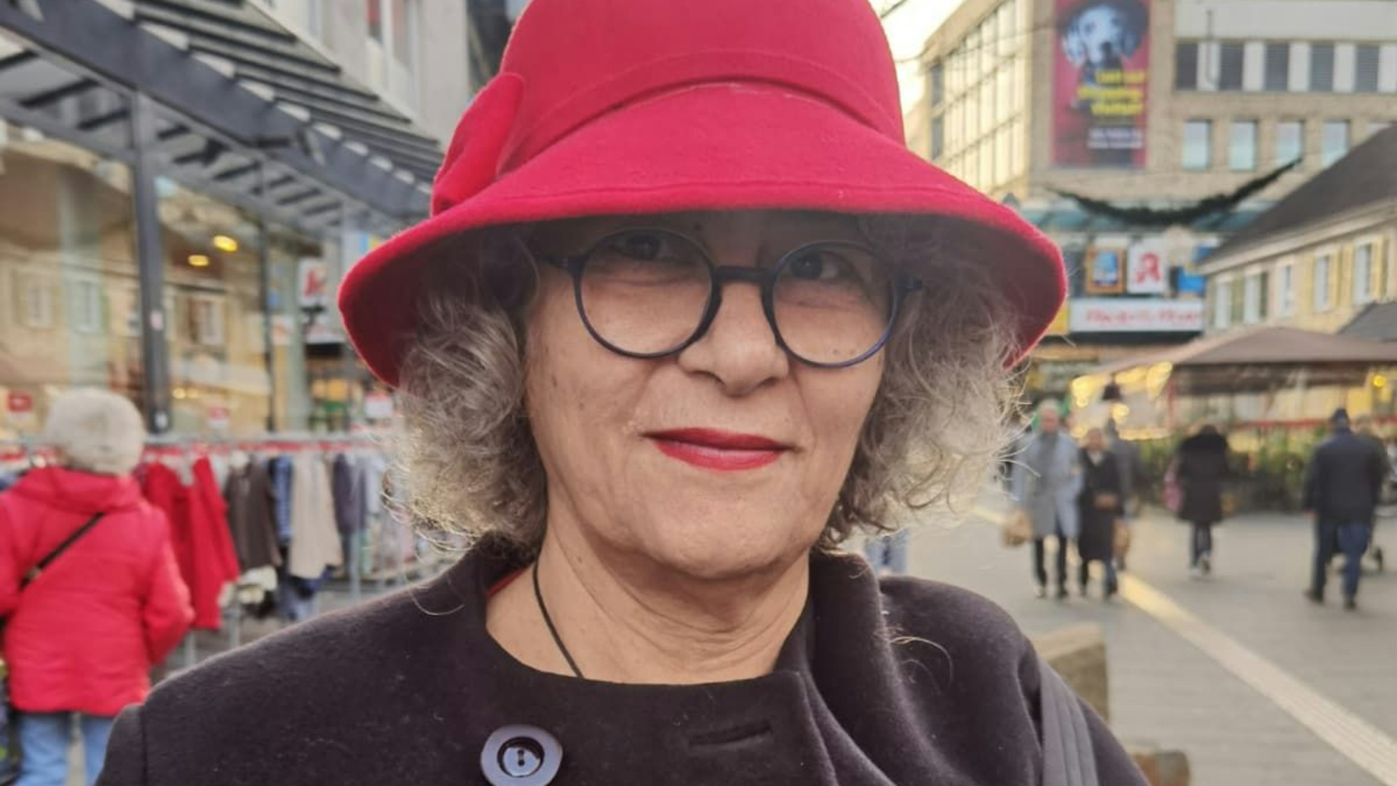 Eine Dame mit rotem Hut und Lippenstift schaut in die Kamera.