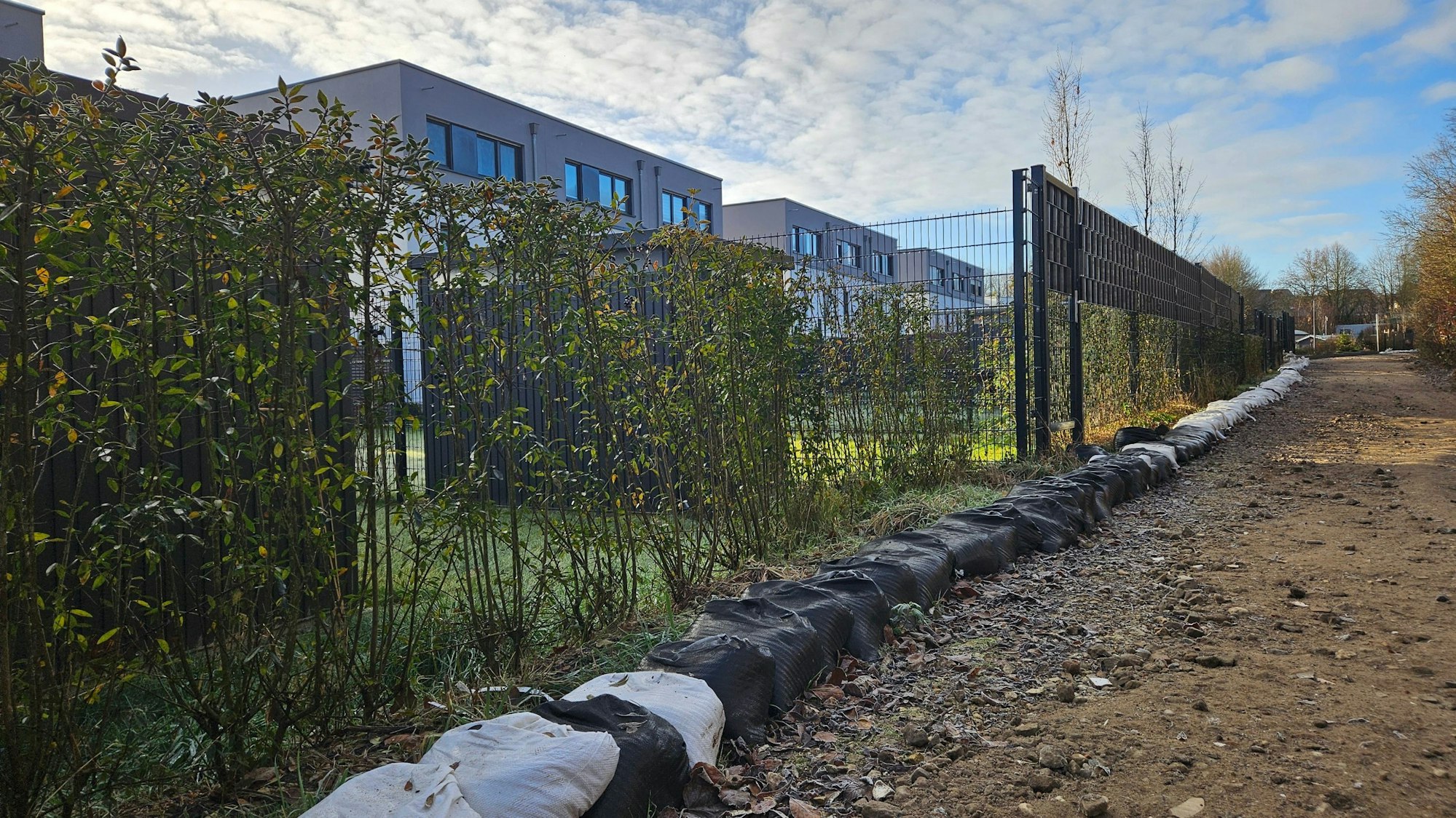 Zu sehen ist eine Reihe Sandsäcke entlang einer Neubausiedlung.