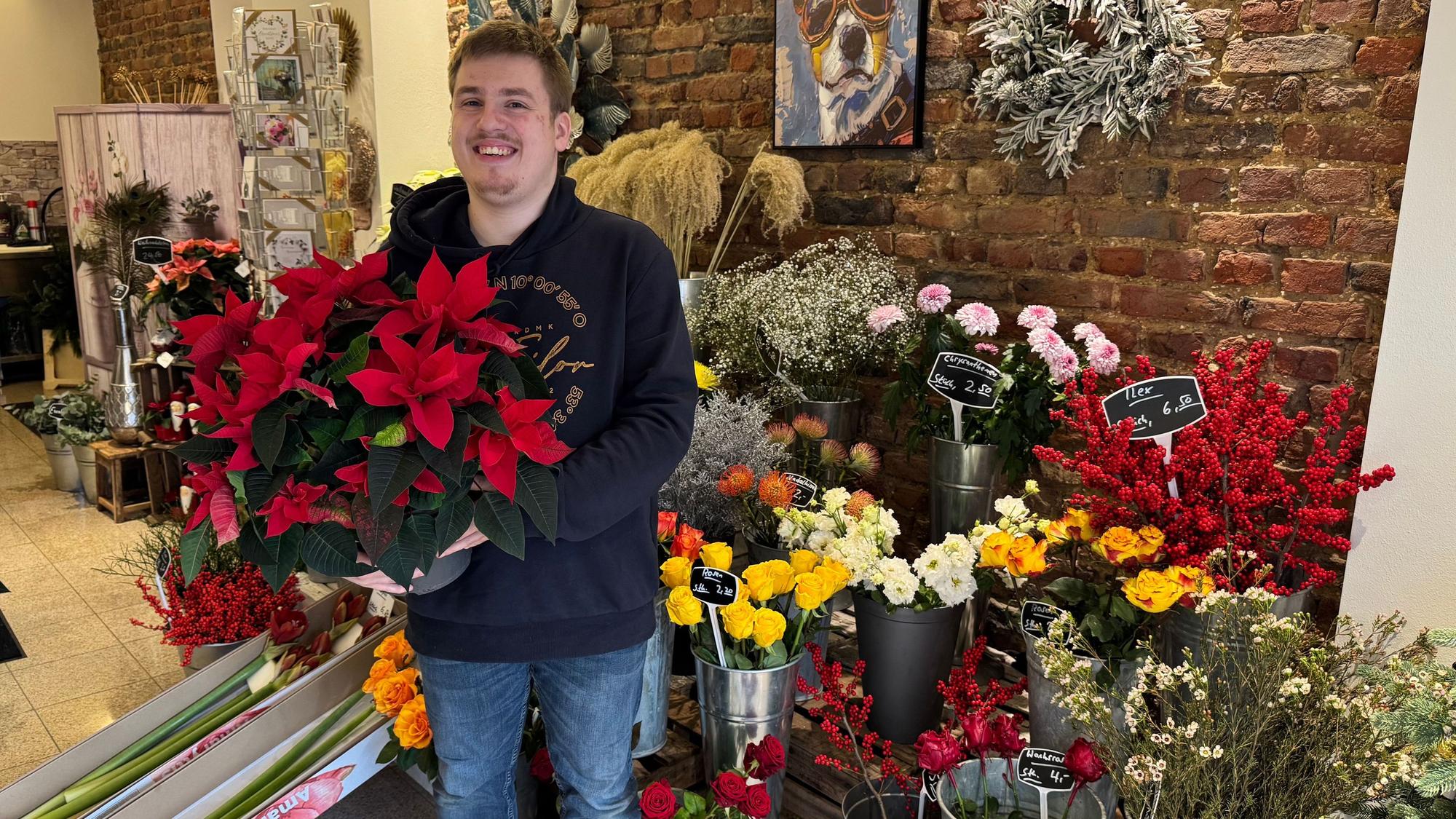 Auf dem Bild ist ein junger Mann in seinem Blumenladen zu sehen.