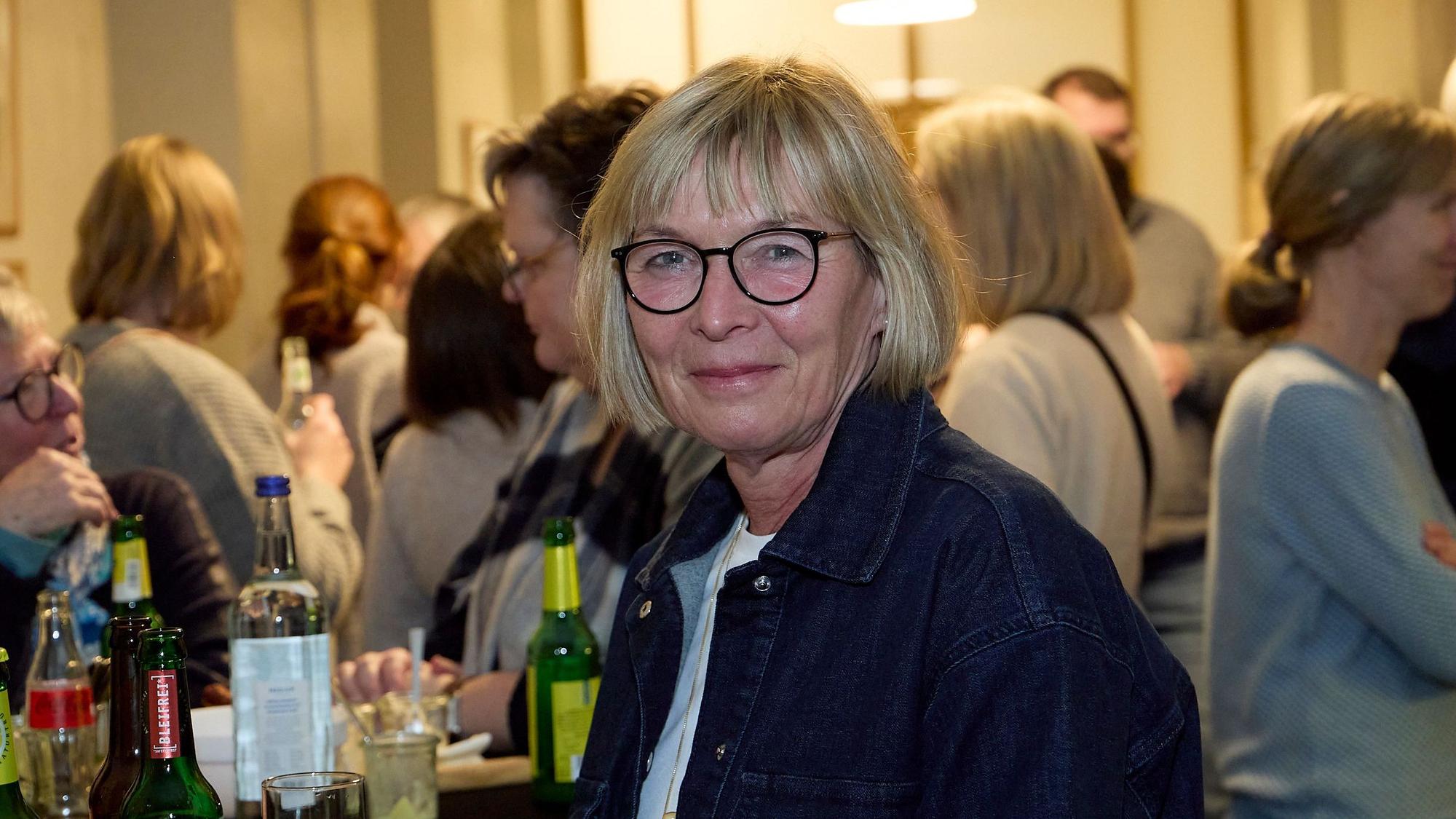 Hildegard Poth steht im Vordergrund, im Hintergrund sind unscharf zahlreiche weitere Menschen zu sehen.