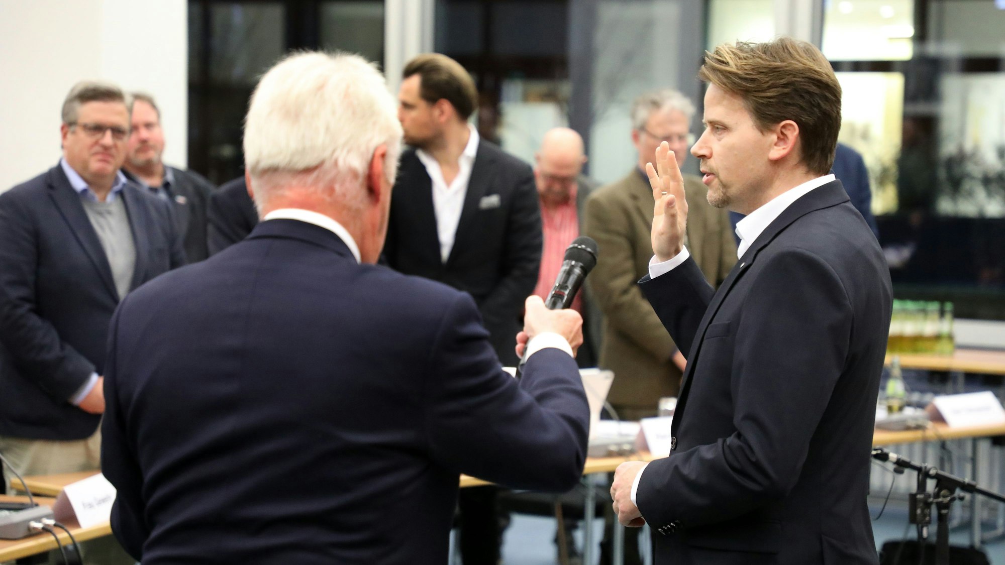 Ein Mann, dem ein Mikrofon an den Mund gehalten wird, hebt die Hand und spricht.