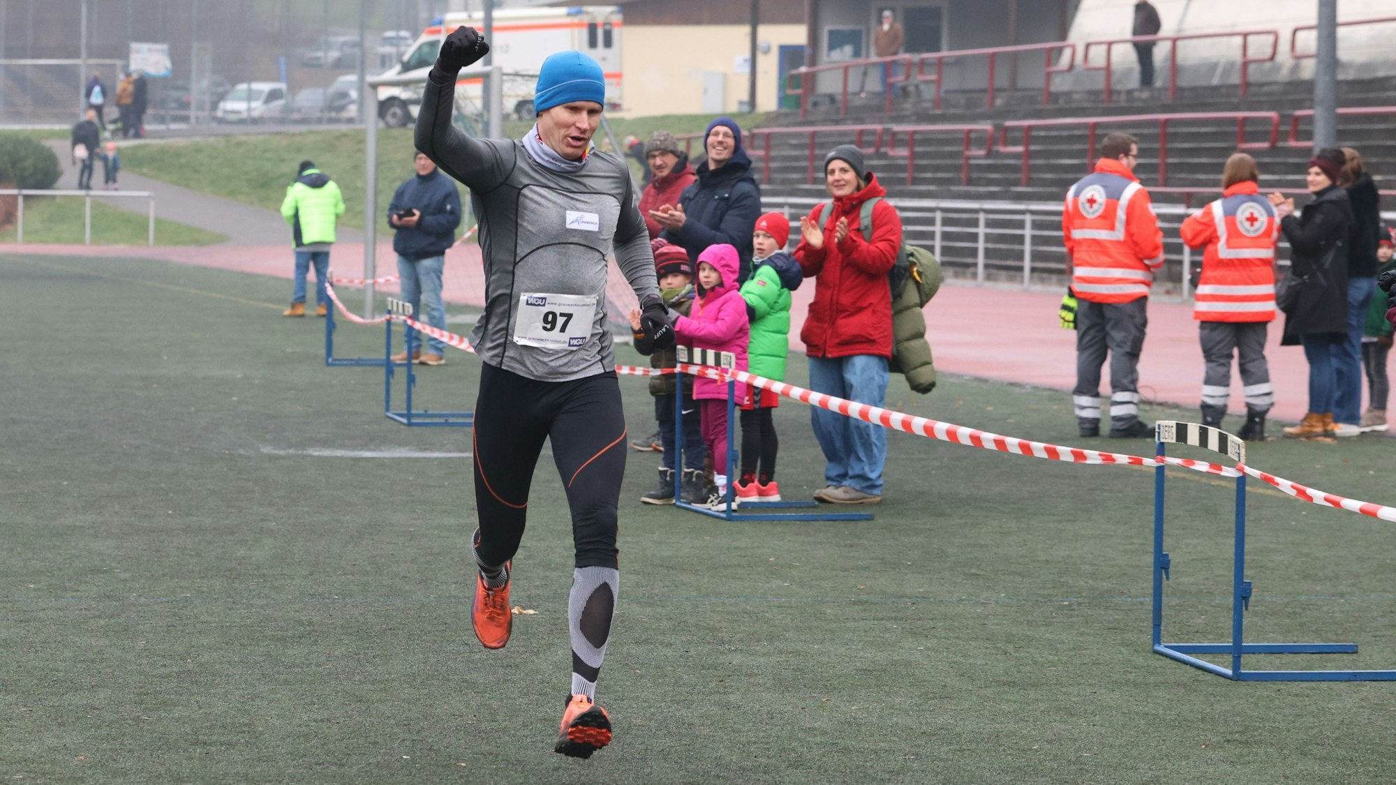 Ein Mann läuft bei einem Crosslauf jubelnd über die Ziellinie.