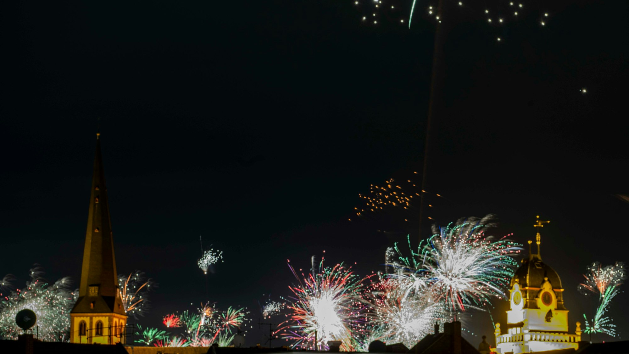Das Bild zeigt zahlreich explodierende Feuerwerksraketen zwischen der Kirche und dem Rathaus.