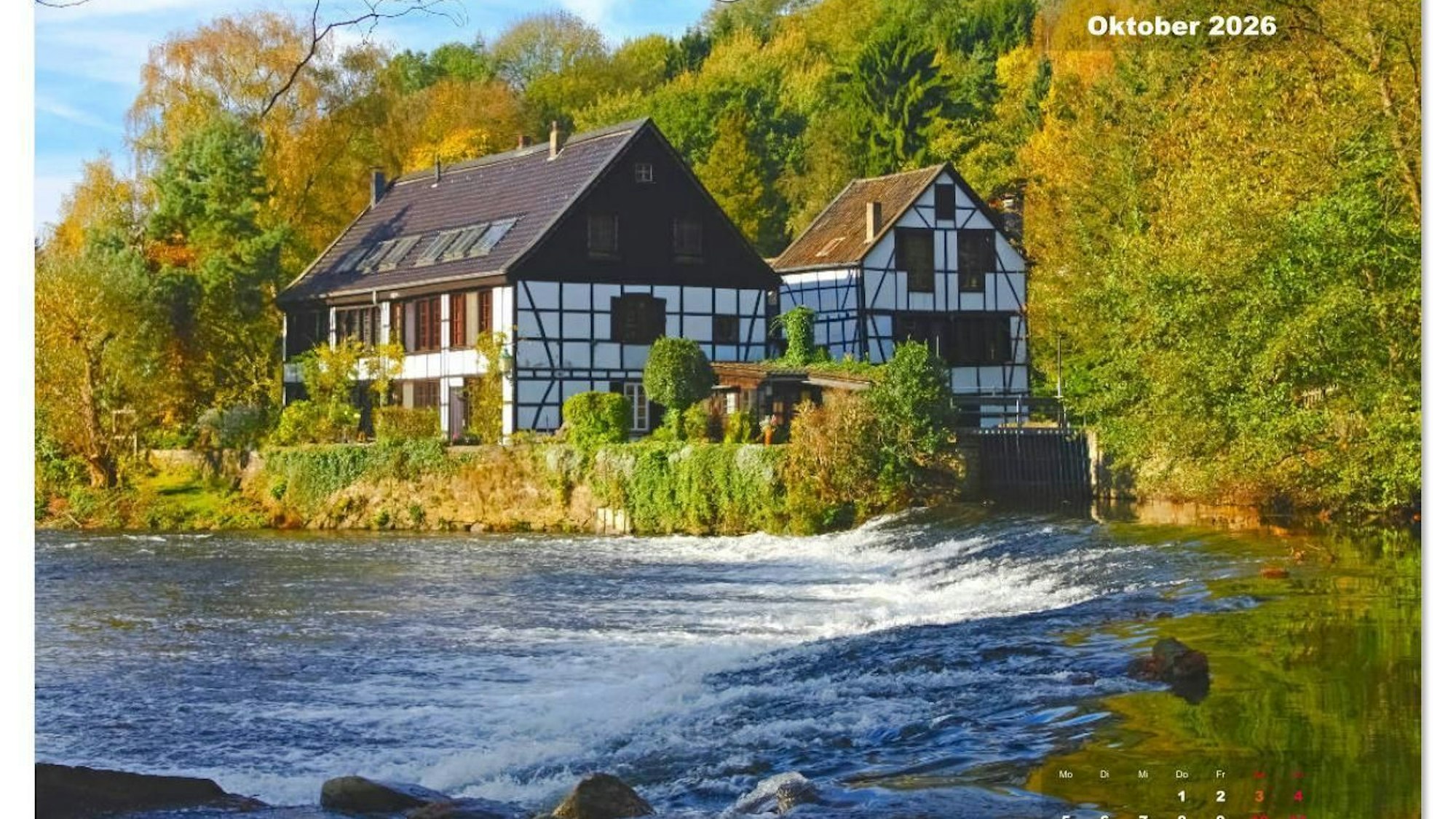 Ein Fachwerkhaus steht vor einem Fluss bei Sonnenschein.