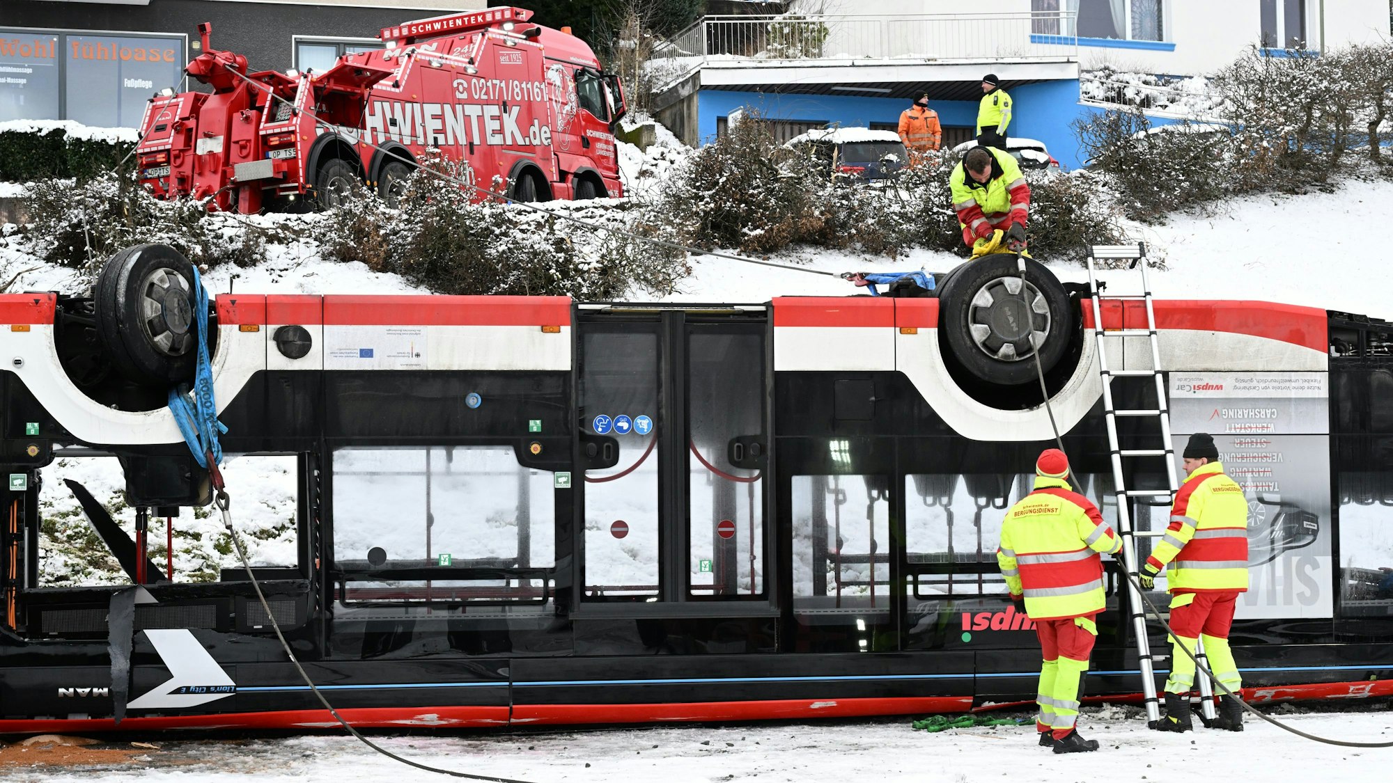 Der Bus liegt auf dem Dach. Zwei Mitarbeiter des Bergungstrupps begutachten das Wrack.