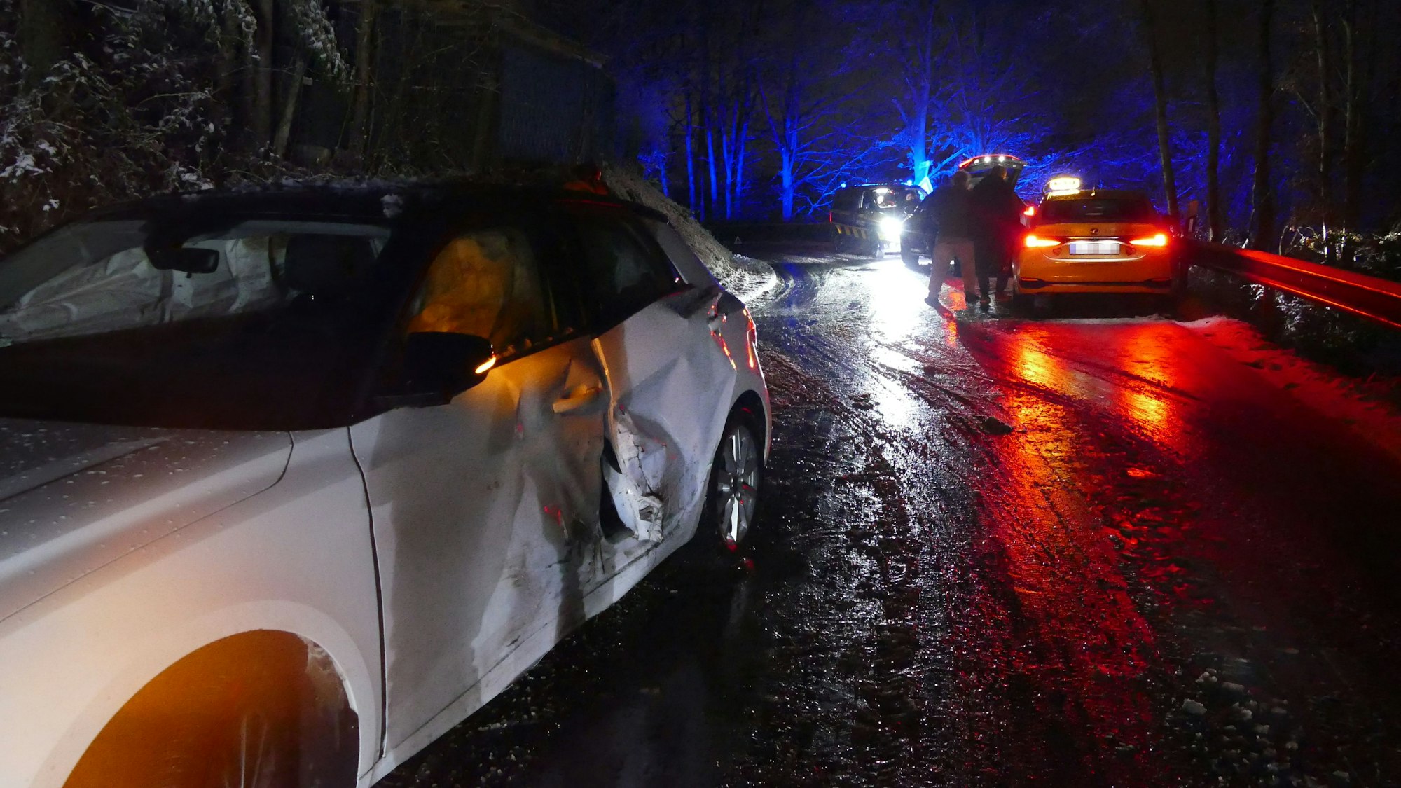 Ein beschädigtes Auto an einer Unfallstelle. Es ist dunkel, die Straße ist nass.