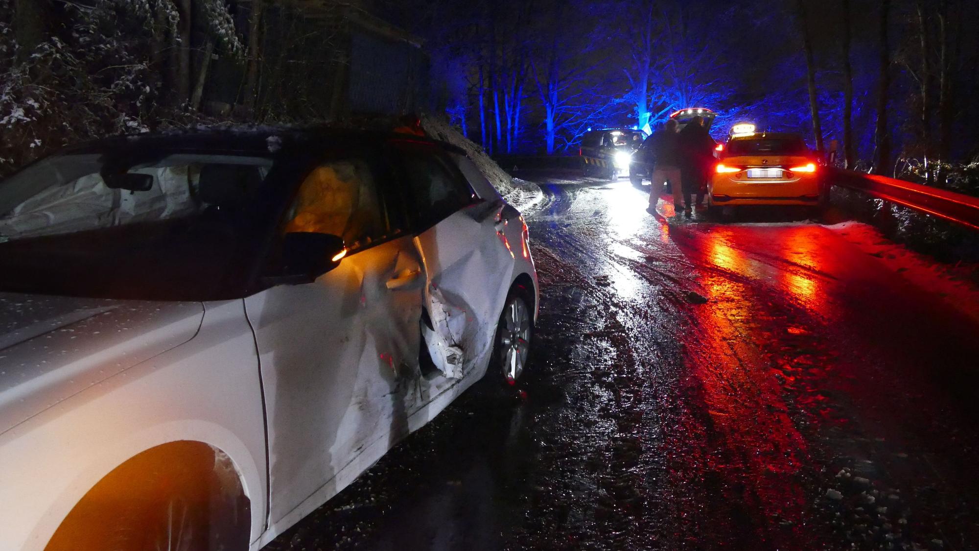 Ein beschädigtes Auto an einer Unfallstelle. Es ist dunkel, die Straße ist nass.