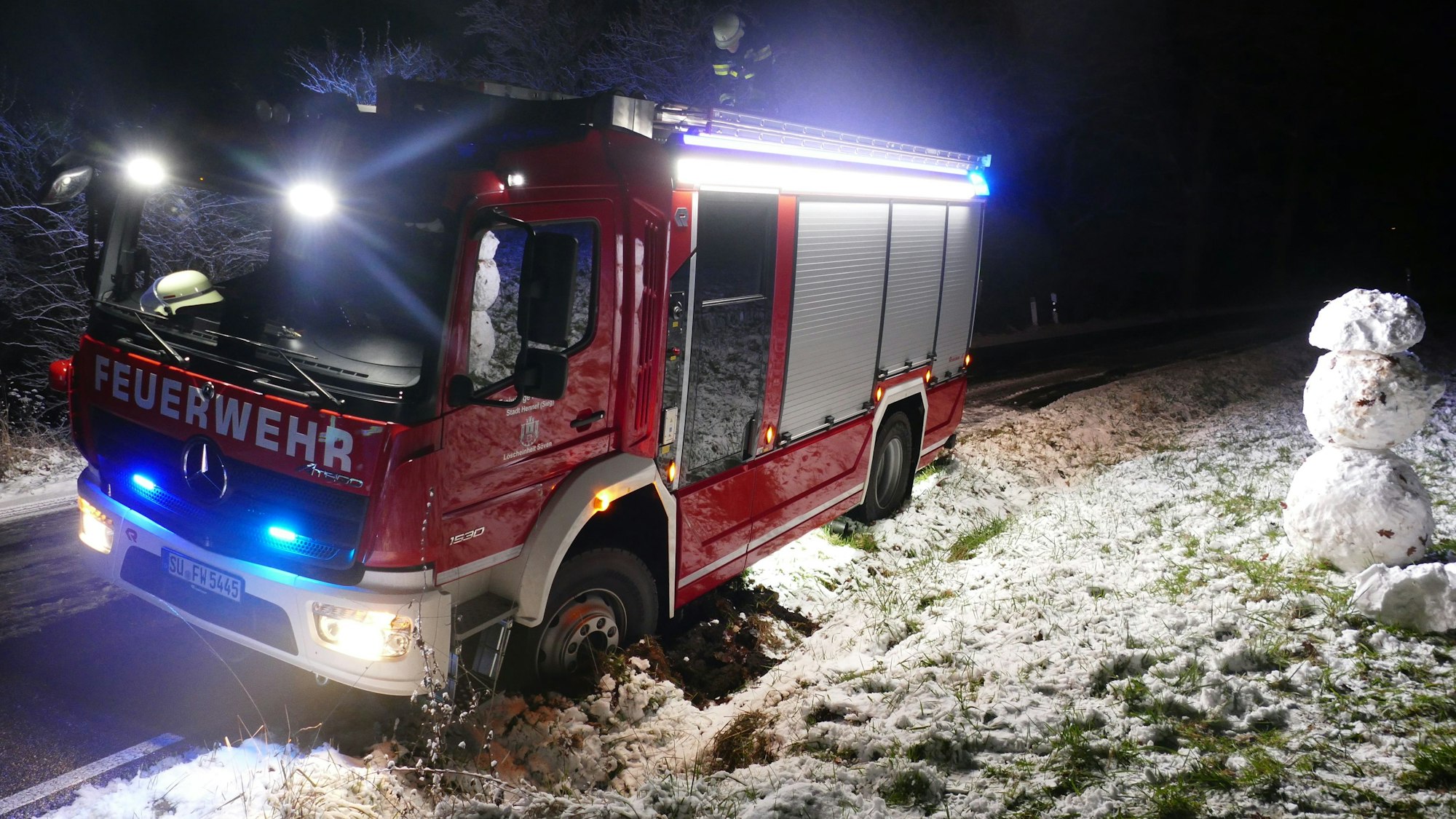 Ein Feuerwehrfahrzeug ist bei Schnee in einen Straßengraben gerutscht.