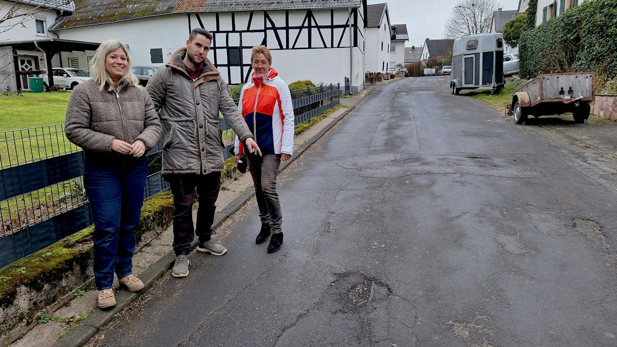 Dirk Dombrofski, der mit den beiden Frauen am Straßenrand steht, zeigt auf ein Schlagloch.