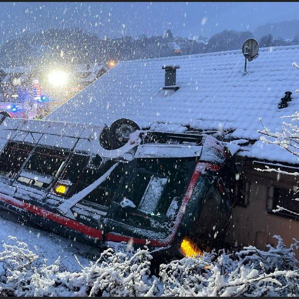 Ein Bus steht auf dem Dach an eine Häuserwand gelehnt. Drum herum liegt Schnee.