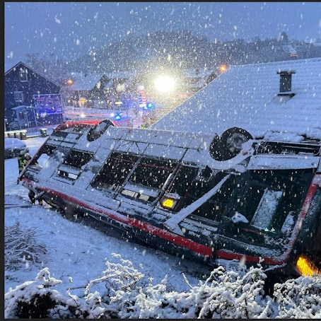 Ein Bus steht auf dem Dach an eine Häuserwand gelehnt. Drum herum liegt Schnee.