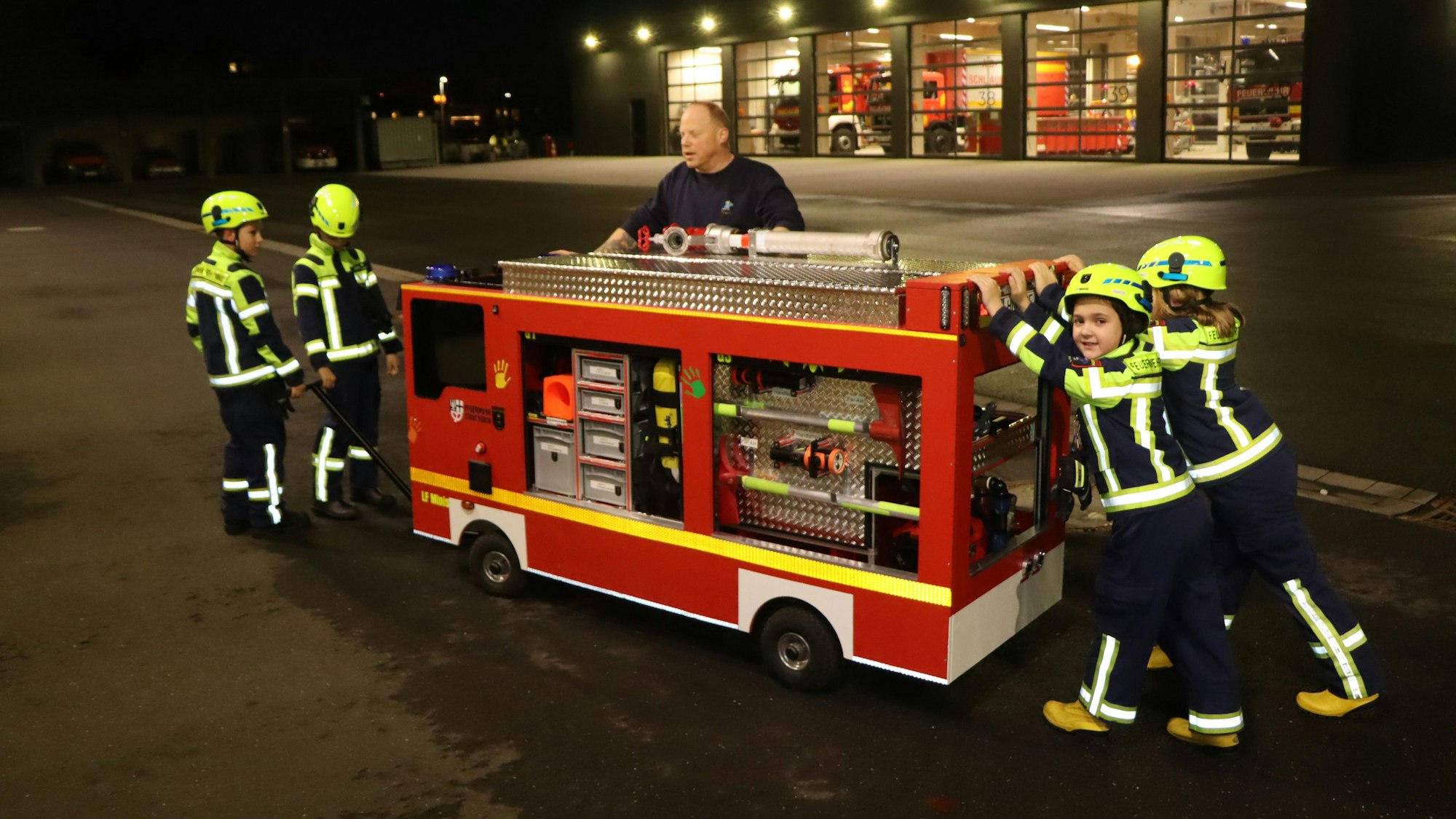 Kinder in Feuerwehruniform ziehen und schieben ein Kinderfeuerwehrauto.