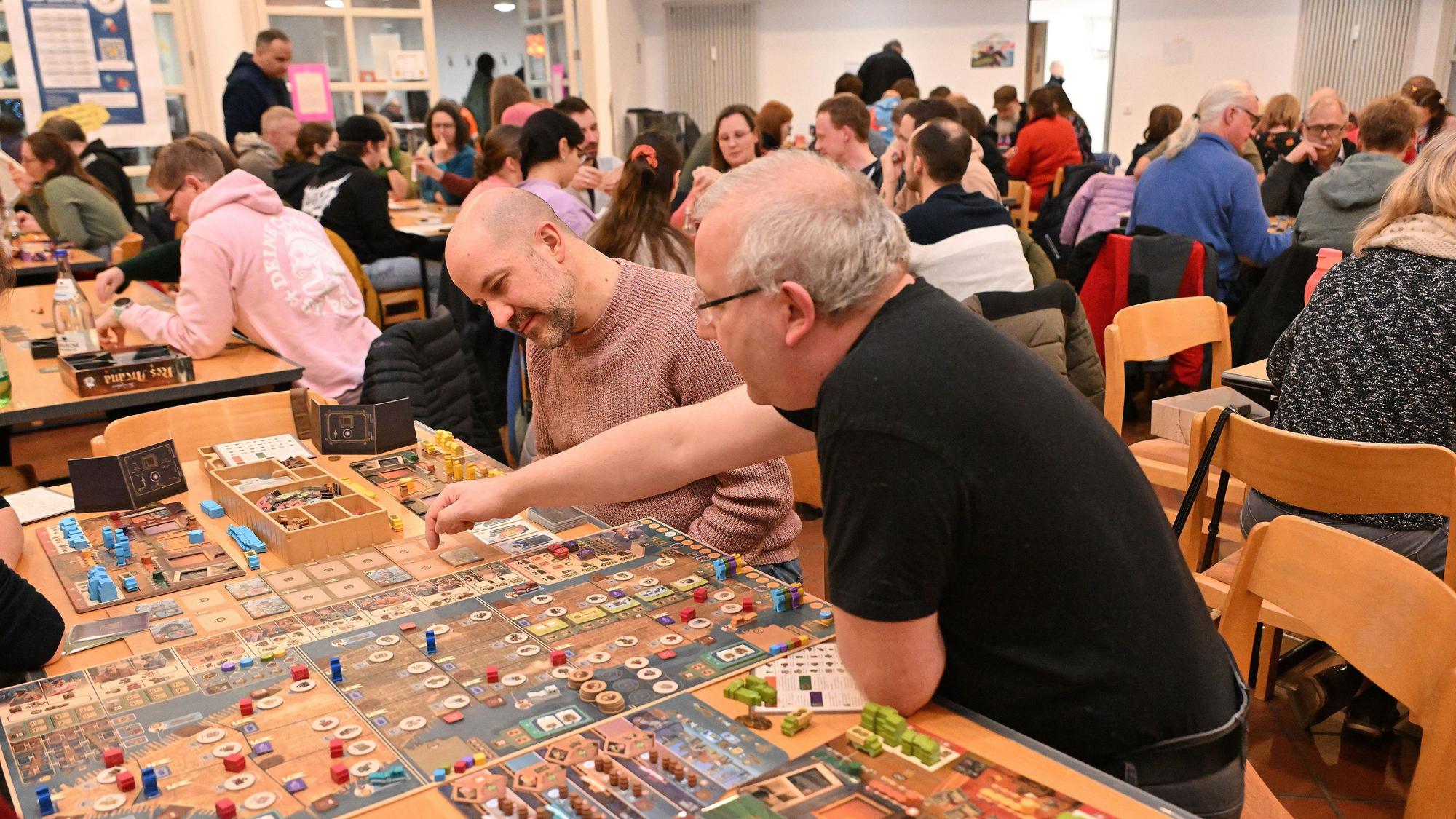 Zwei Männer sitzen an einem Brettspiel und überlegen.