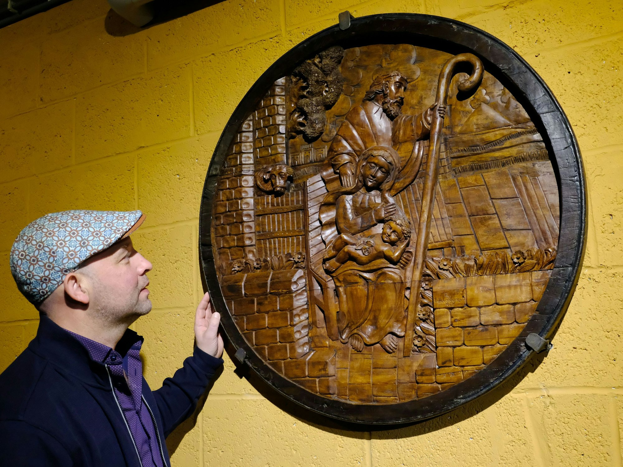 Michael Balter steht an einer runden Holzschnitzerei, die eine Krippendarstellung zeigt.