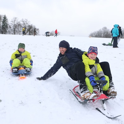 Ein Vater rodelt mit seinen beiden Kindern.