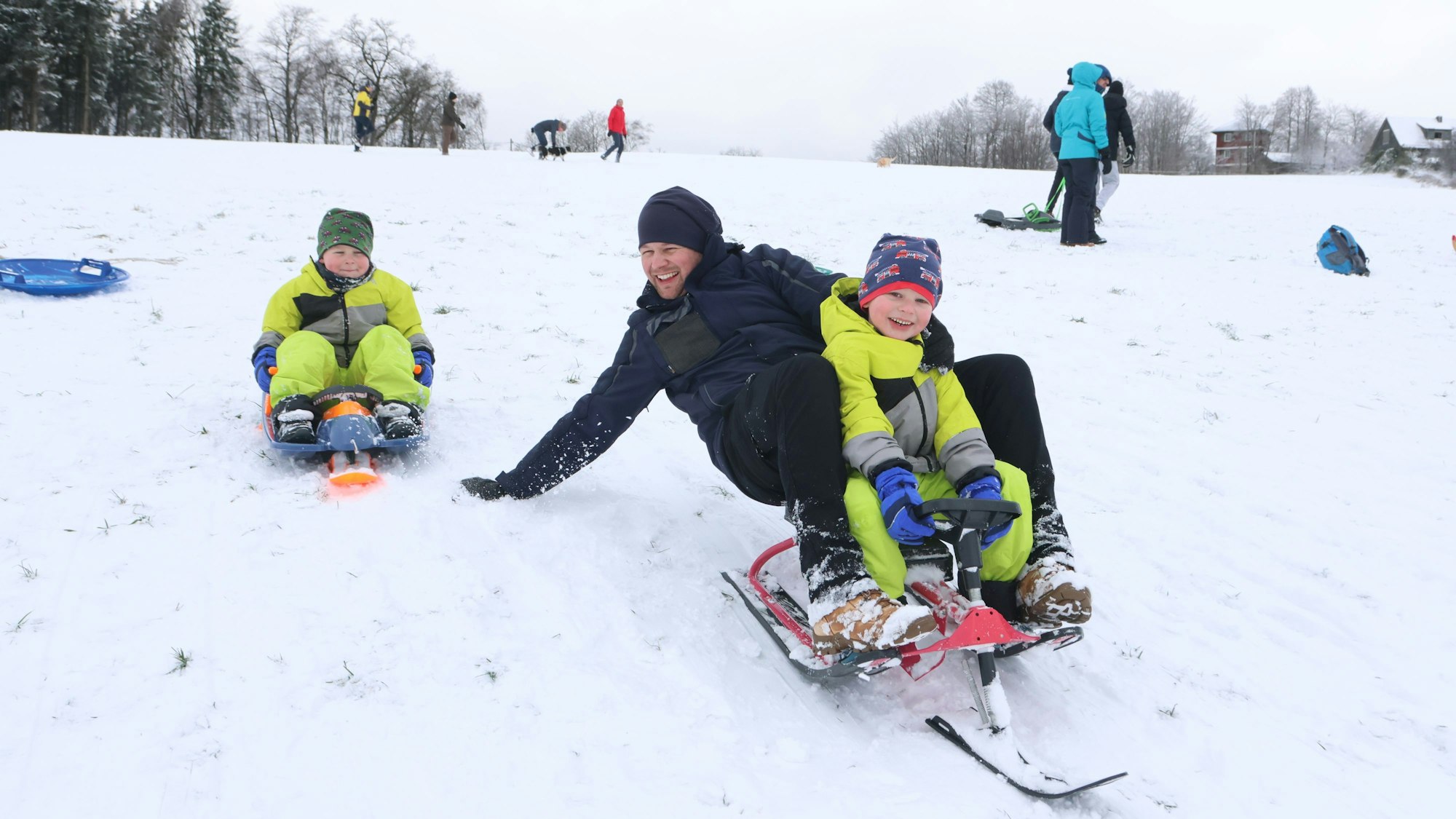 Ein Vater rodelt mit seinen beiden Kindern.