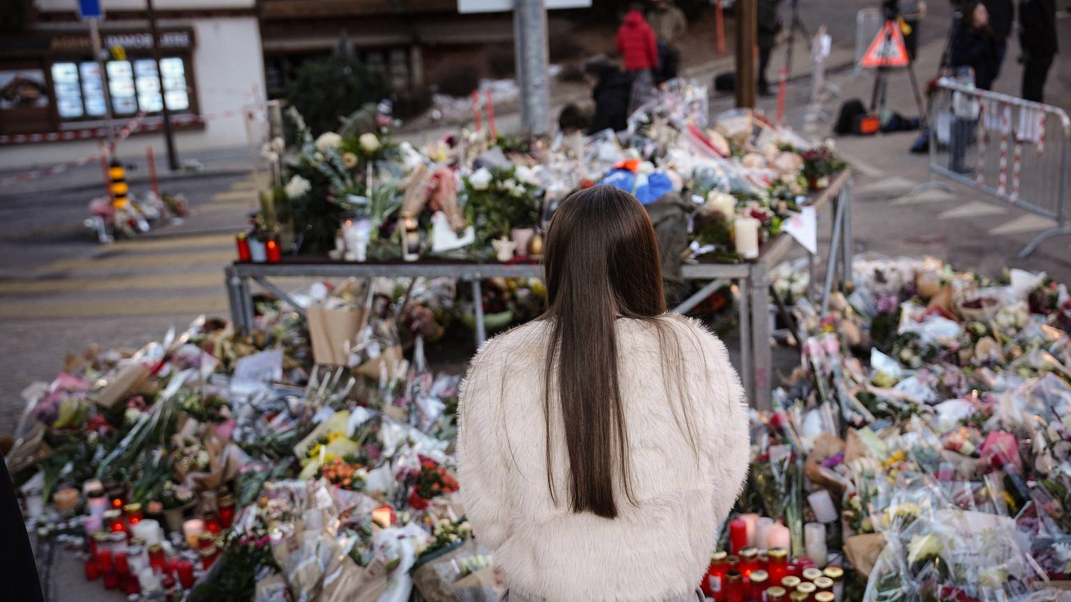 Eine junge Frau steht vor Blumen in Crans-Montana. Unter den Opfern der Brandkatastrophe sind auch Teenager.
