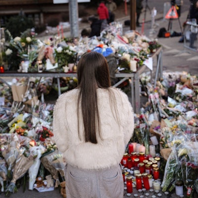 Eine junge Frau steht vor Blumen in Crans-Montana. Unter den Opfern der Brandkatastrophe sind auch Teenager.