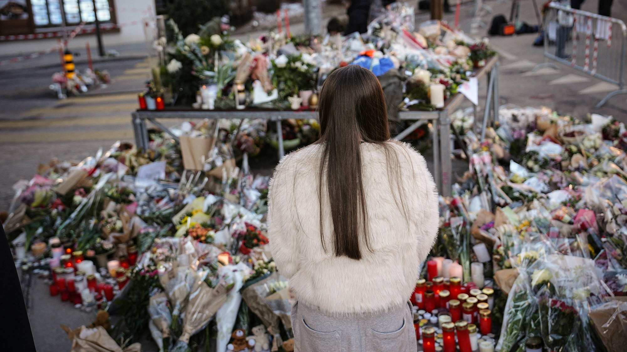 Eine junge Frau steht vor Blumen in Crans-Montana. Unter den Opfern der Brandkatastrophe sind auch Teenager.