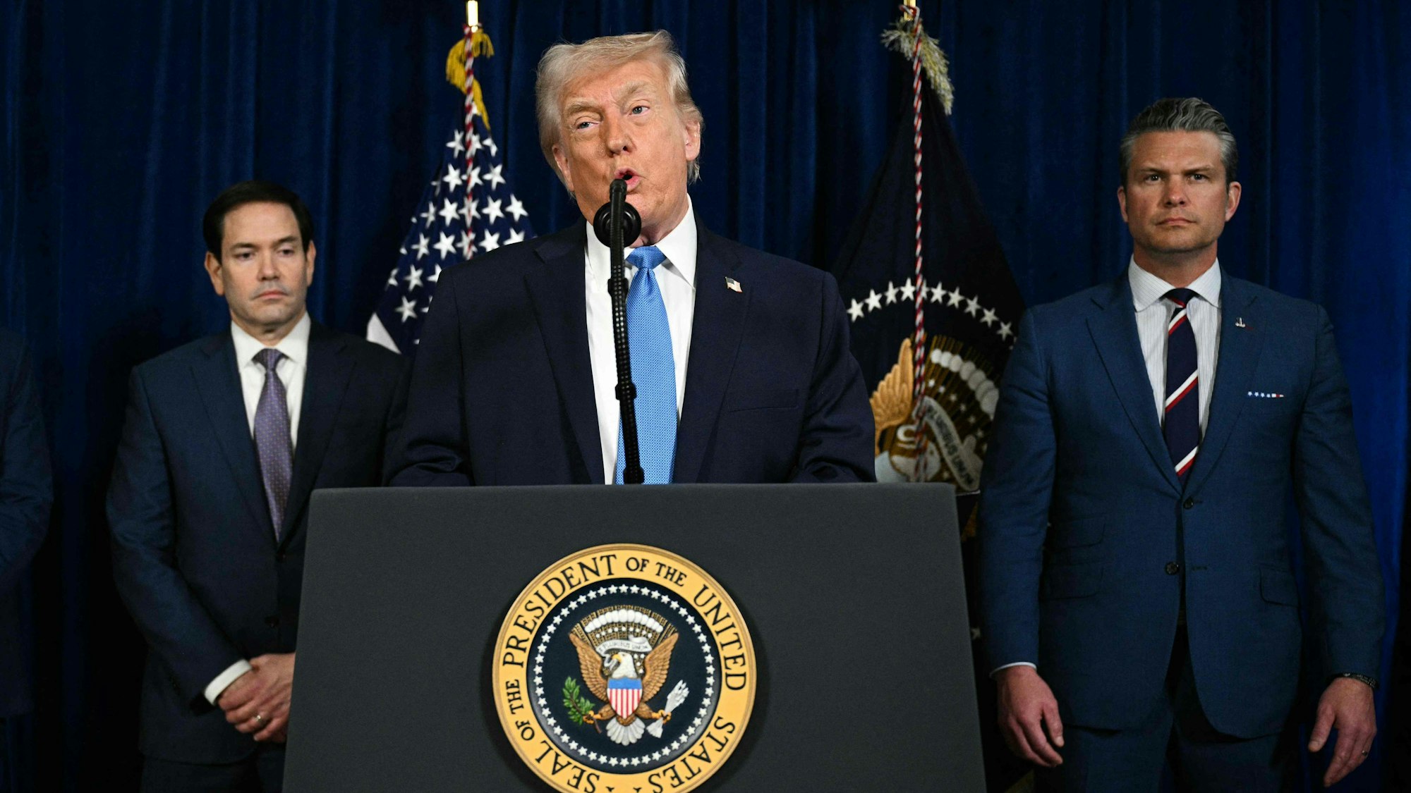 US-Präsident Donald Trump bei einer Pressekonferenz am Samstag (3. Januar) in Mar-a-Lago. Im Hintergrund sind US-Außenminister Marco Rubio (l.) und Verteidigungsminister Pete Hegseth zu sehen.