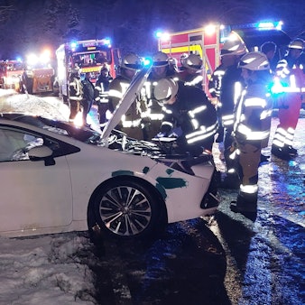 Ein beschädigtes Auto an einer Unfallstelle. Es ist dunkel, die Straße ist nass.