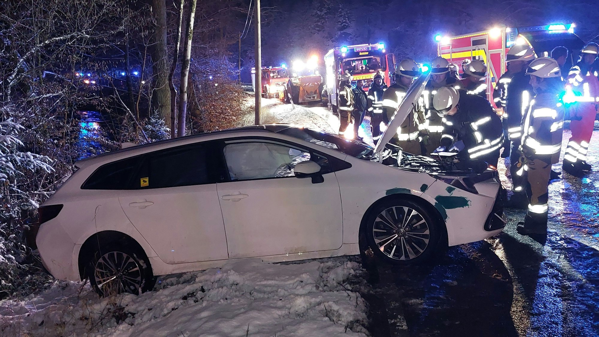 Ein beschädigtes Auto an einer Unfallstelle. Es ist dunkel, die Straße ist nass.