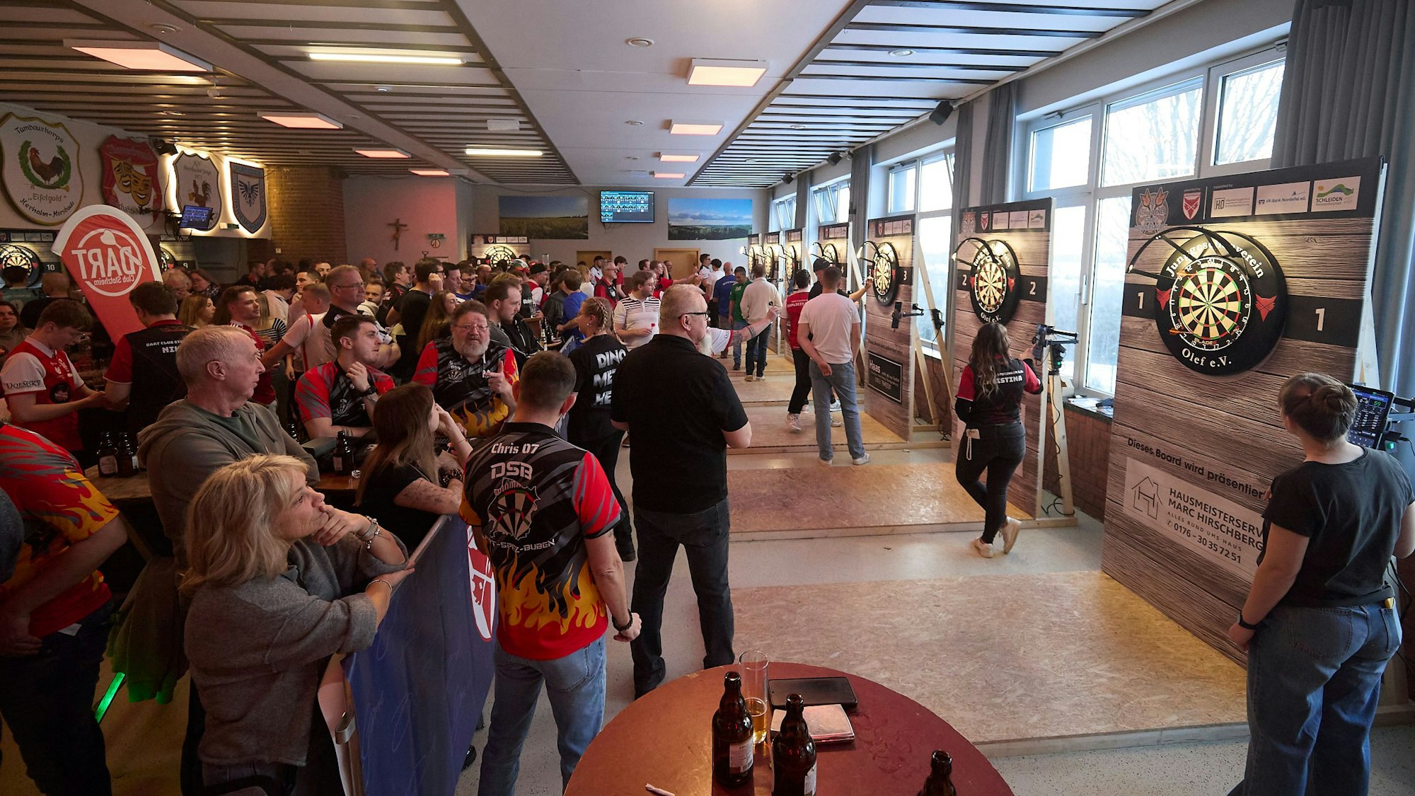 Blick in das voll besetzte Bürgerhaus mit mehreren Dart-Scheiben.
