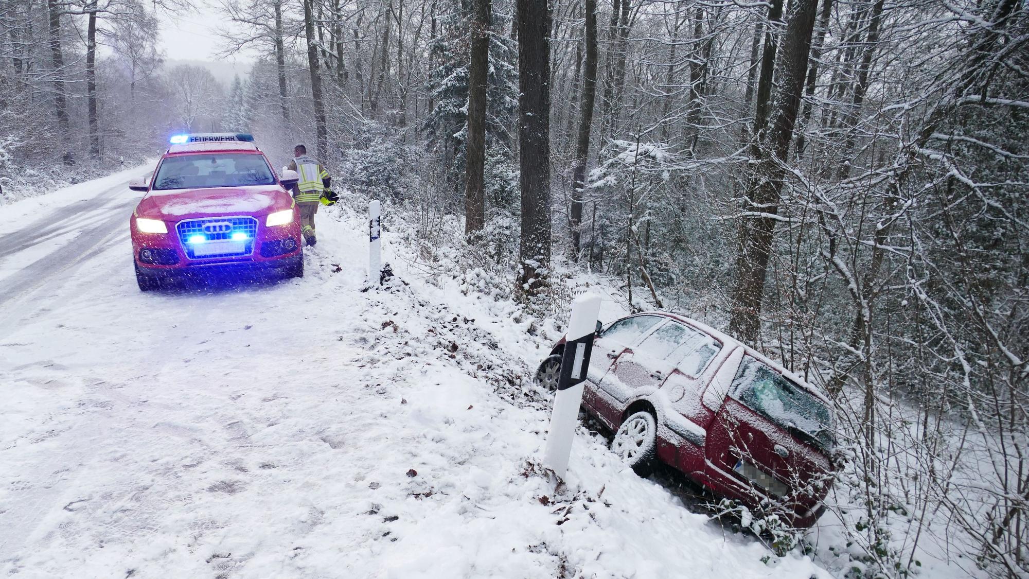 Ein Auto ist von der schneeglatten Fahrbahn abgekommen und liegt in einem Abhang im Wald.