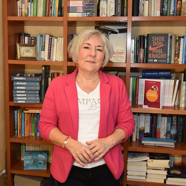Die Autorin steht vor einem Bücherregal.