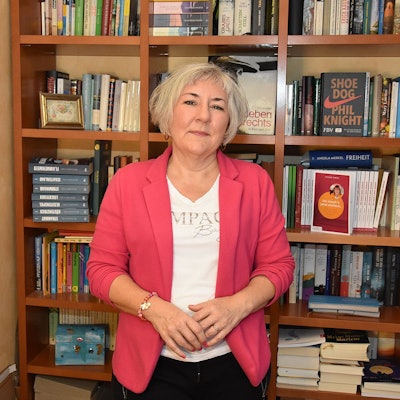 Die Autorin steht vor einem Bücherregal.