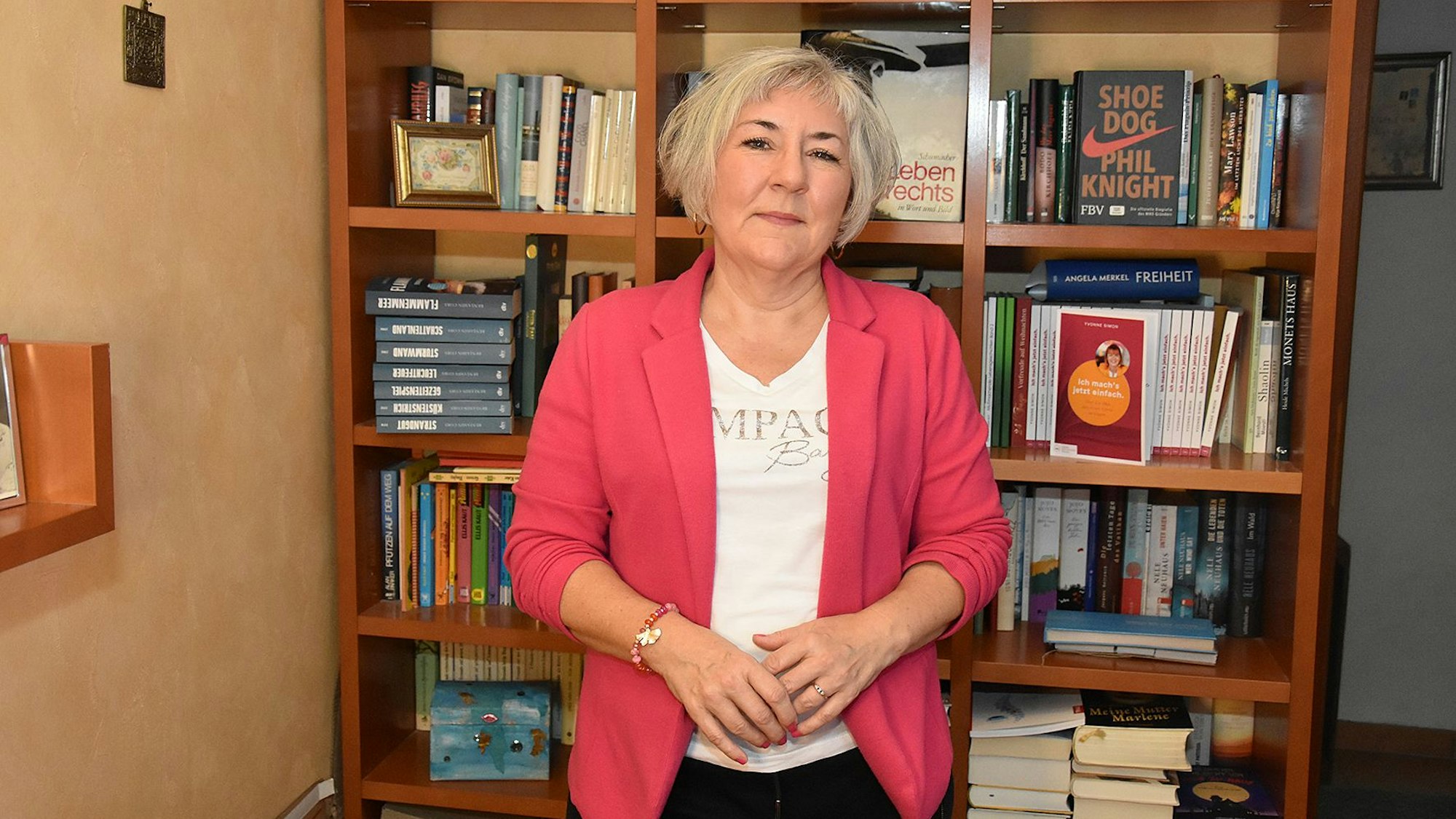Die Autorin steht vor einem Bücherregal.
