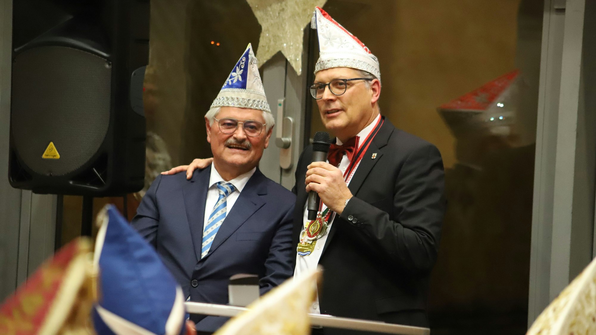 Reinhard Gotzen steht neben Bürgermeister Ulf Hürtgen. Der Bürgermeister hält ein Mikrofon in der linken Hand und hat seine rechte Hand auf Gotzens Schulter abgelegt.