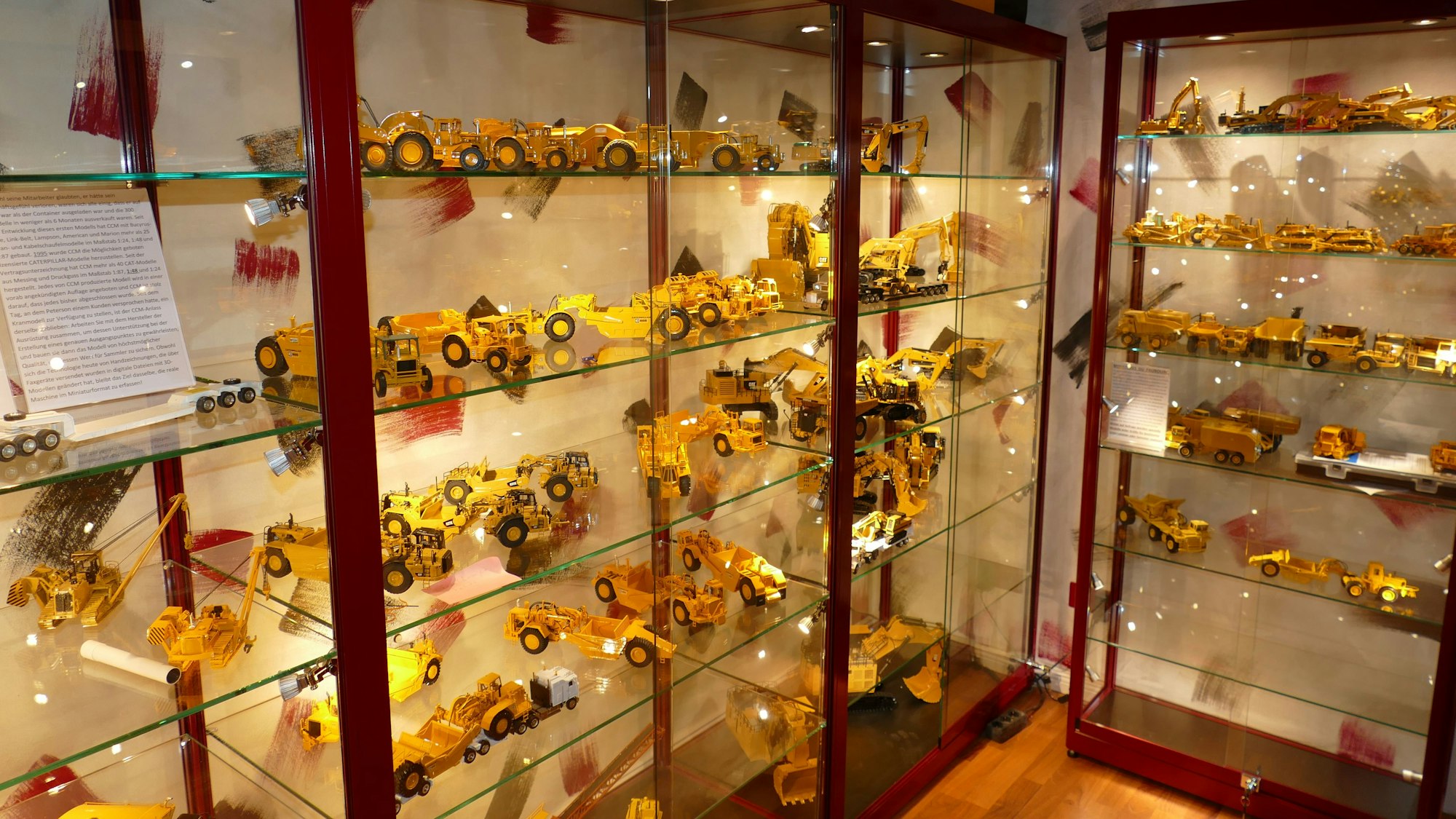 Caterpillar-Modellbaufahrzeuge stehen ausgeleuchtet in einer dunkelroten Vitrine.