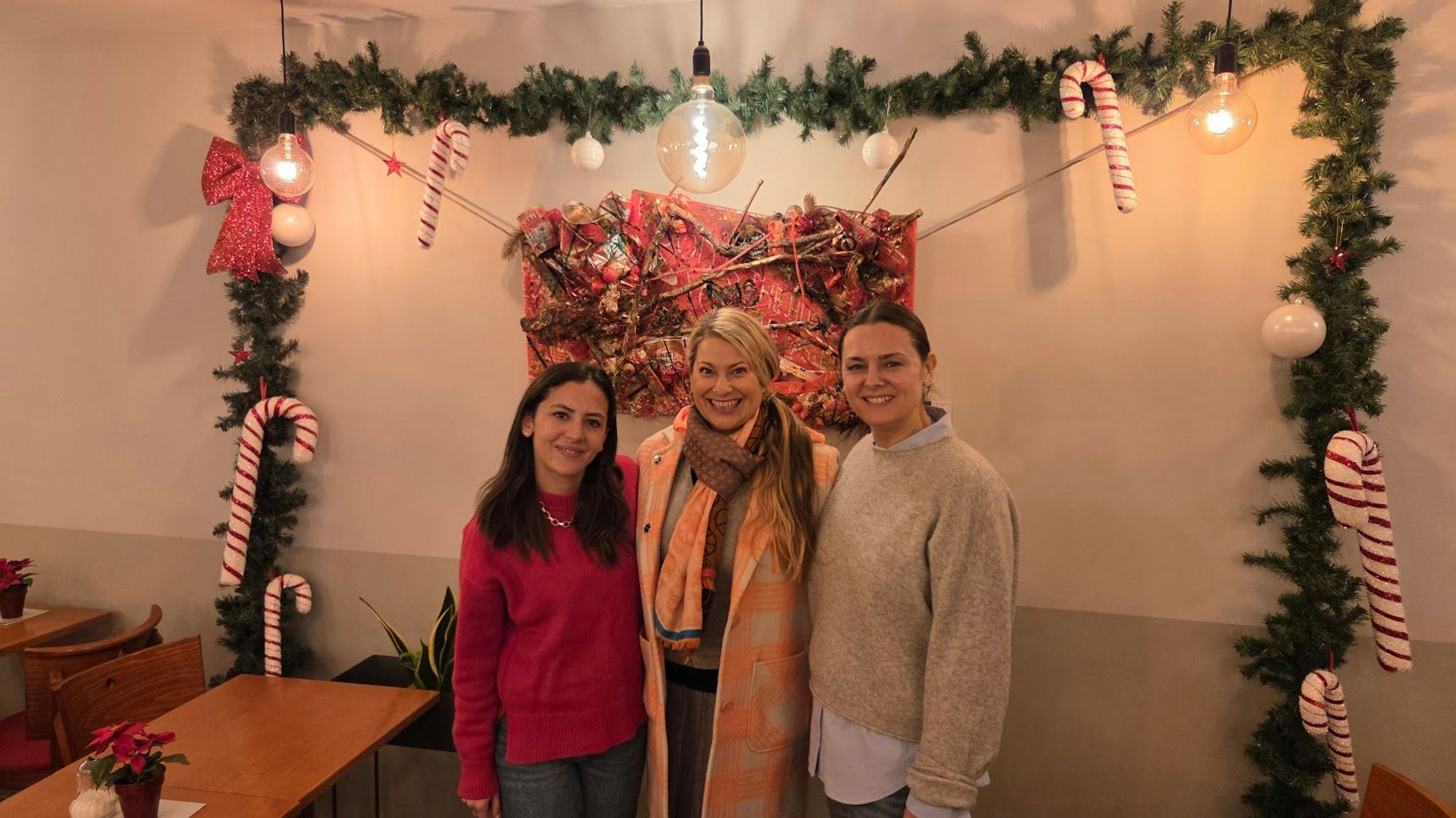 Künstlerin Manuela Klein (Mitte) vor ihrem Kunstwerk im Café „Printen Schmitz“ mit Inhaberinnen Vivienne Schmitz und Simone Schmitz (v.l.)