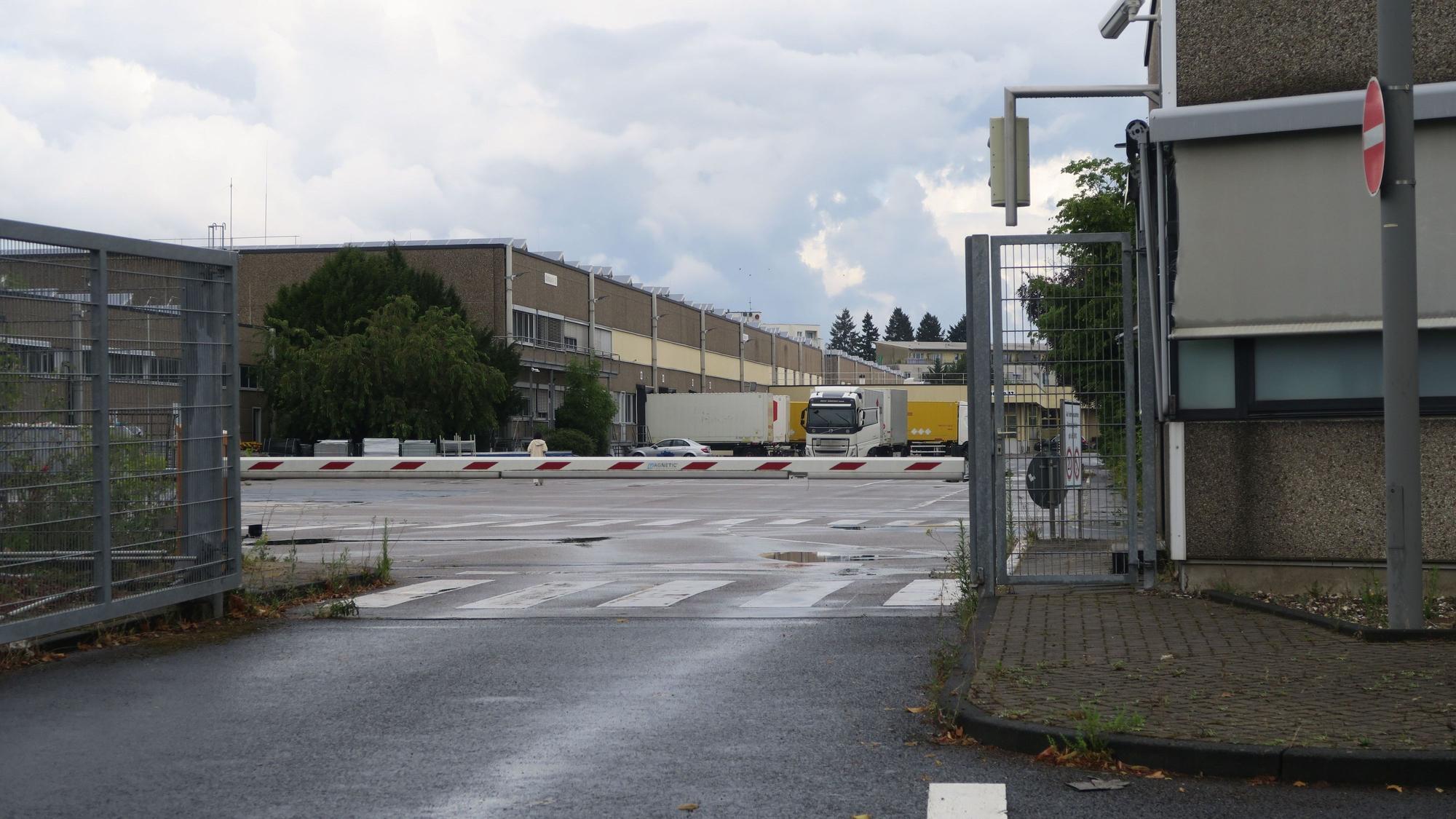 Hinter einem Schlagbaum ist der Betriebshof eines Firmengeländes zu sehen.