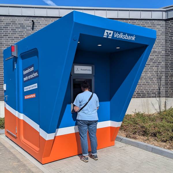 Zu sehen sind der blau-orange Pavillon und ein Kunde am Automaten.