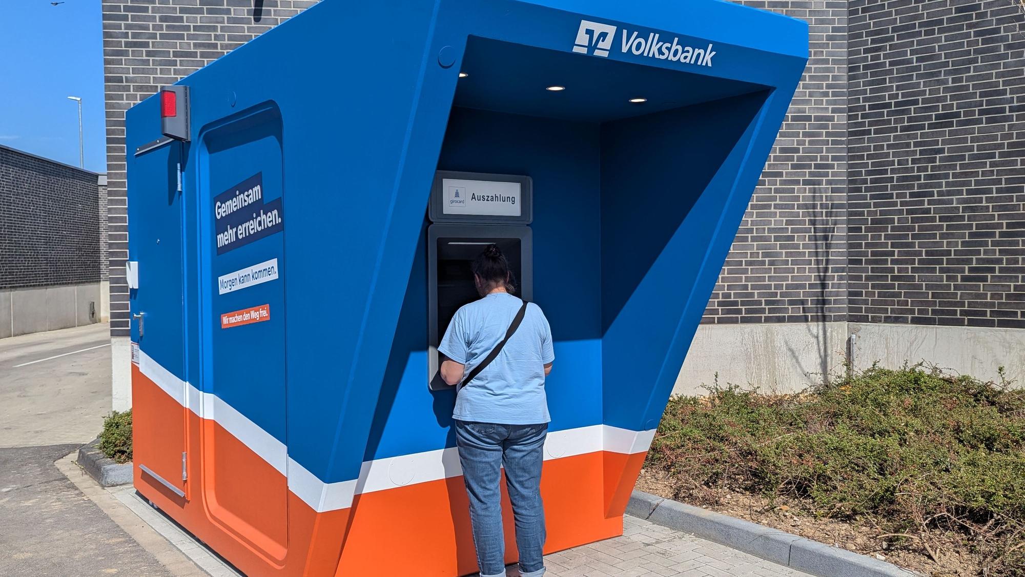Zu sehen sind der blau-orange Pavillon und ein Kunde am Automaten.