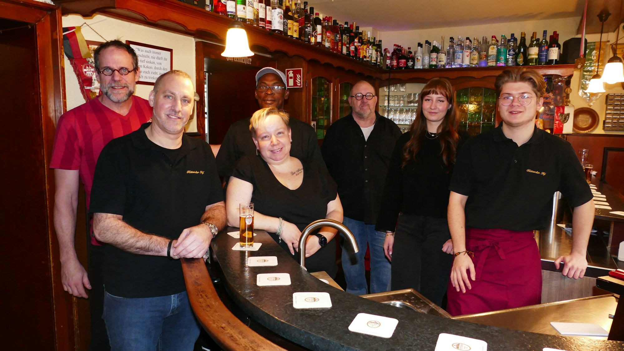 Sieben Menschen stehen an und hinter der Theke einer Kneipe.