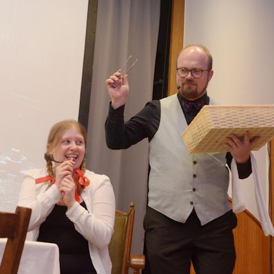 Magdalena Bork sitzt am Tisch, Gregor Weichsel steht in der Rolle des Butlers neben ihr.