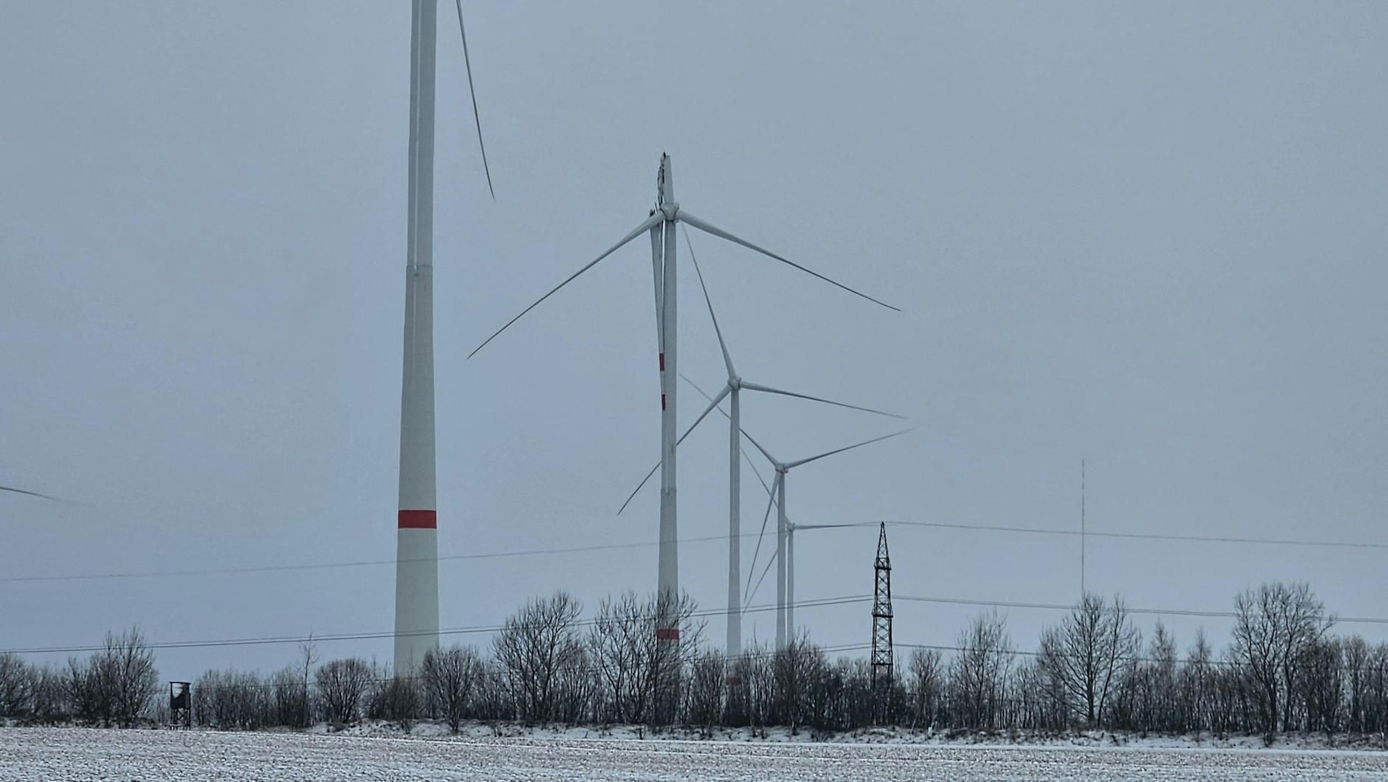 Das Bild zeigt mehrere Windenergieanlagen, darunter auch die defekte mit abgeknicktem Rotorblatt.