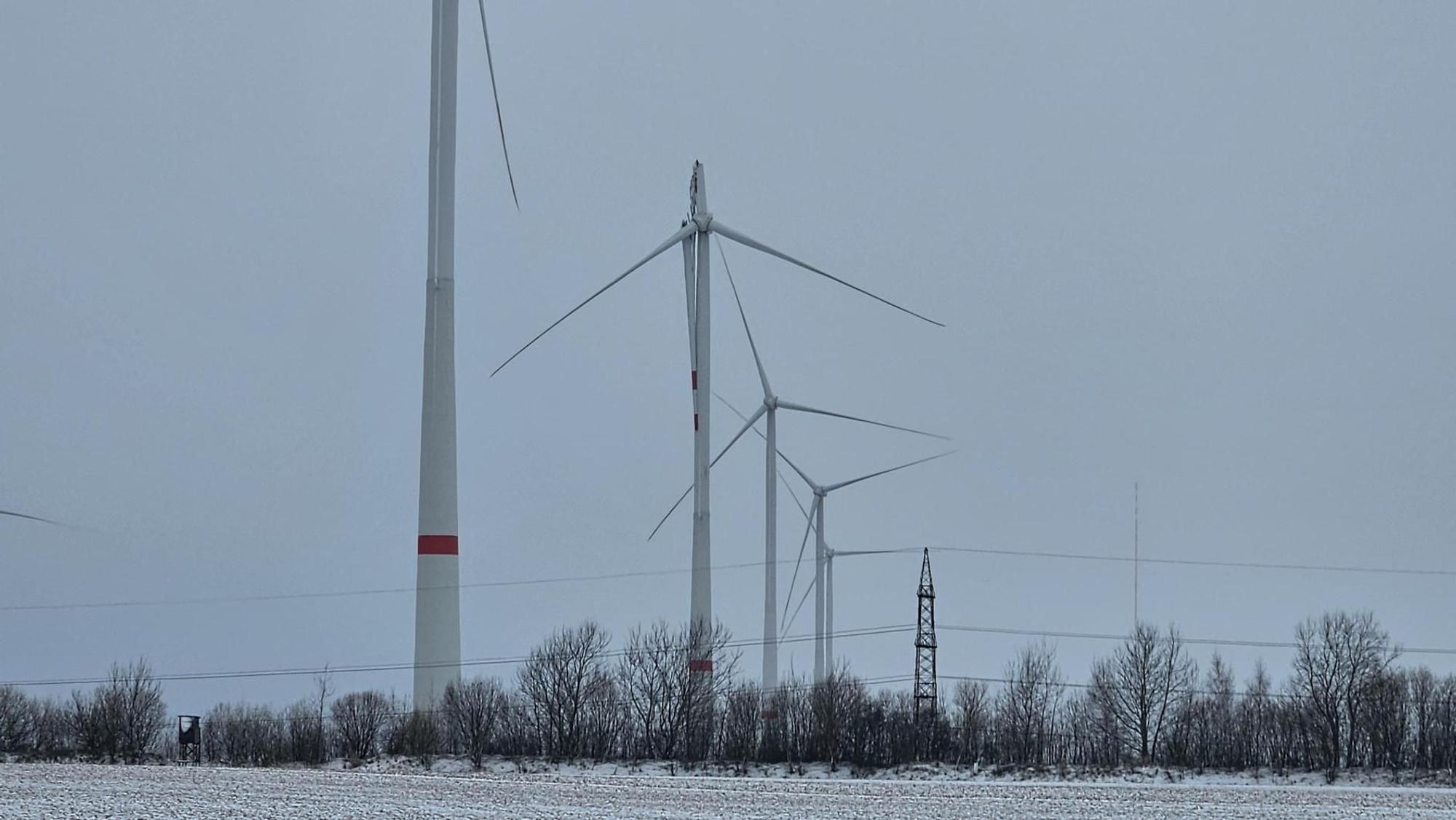 Das Bild zeigt mehrere Windenergieanlagen, darunter auch die defekte mit abgeknicktem Rotorblatt.