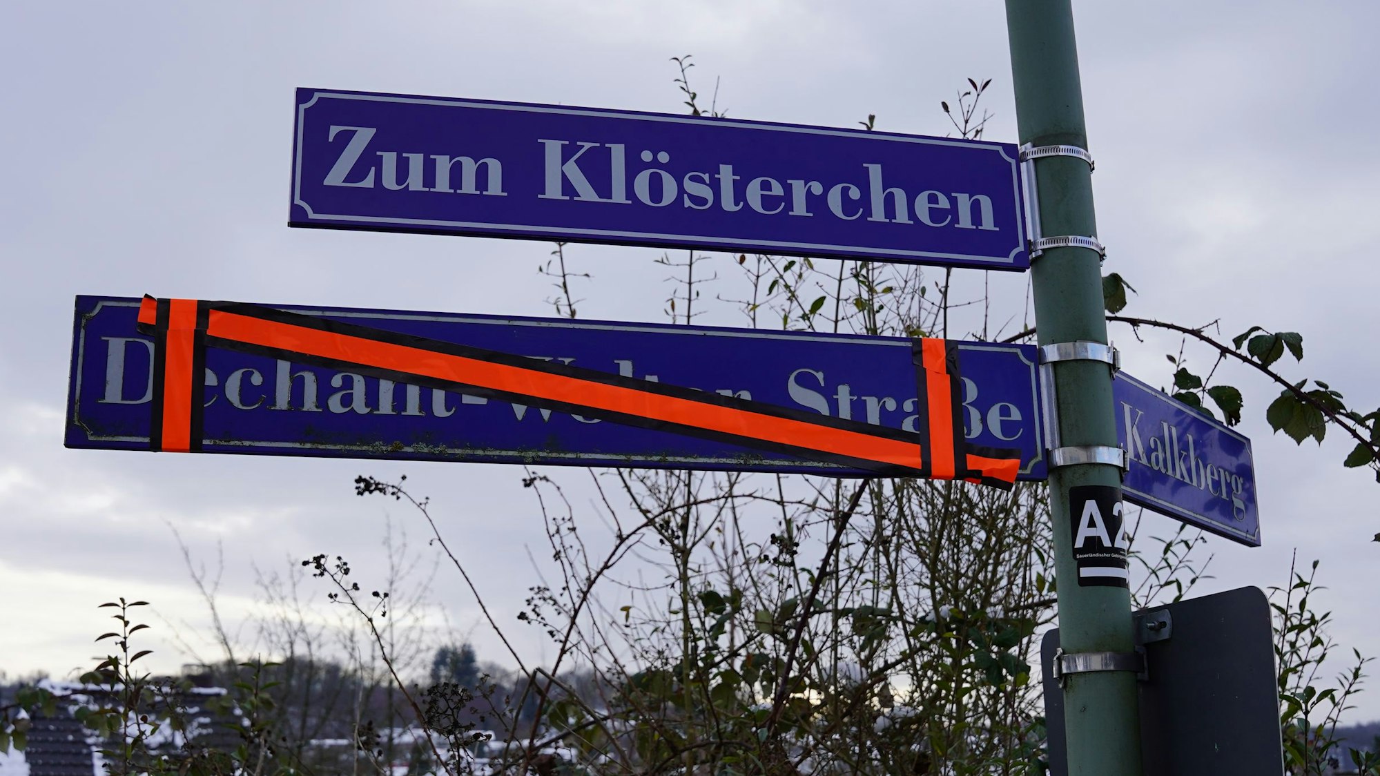 Der neue Straßenname „Zum Klösterchen“ hängt, noch ein Jahr aber soll in der Stadtmitte von Waldbröl auch das alte, inzwischen überklebte Schild sichtbar sein. Dieses erinnert an den Pfarrer und Dechant Emmerich Wolter. Dem Verstorbenen wird der sexuelle Missbrauch an Kindern vorgeworfen.