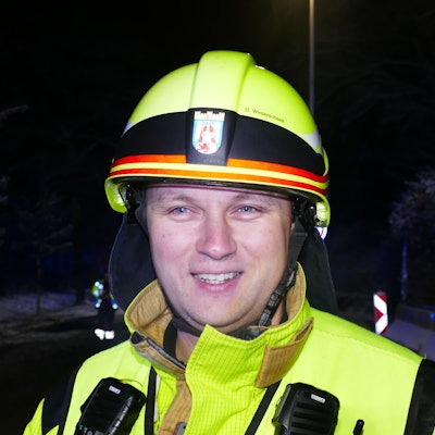 Ein Mann mit gelbem Feuerwehrhelm und einer gelb reflektierenden Jacke.