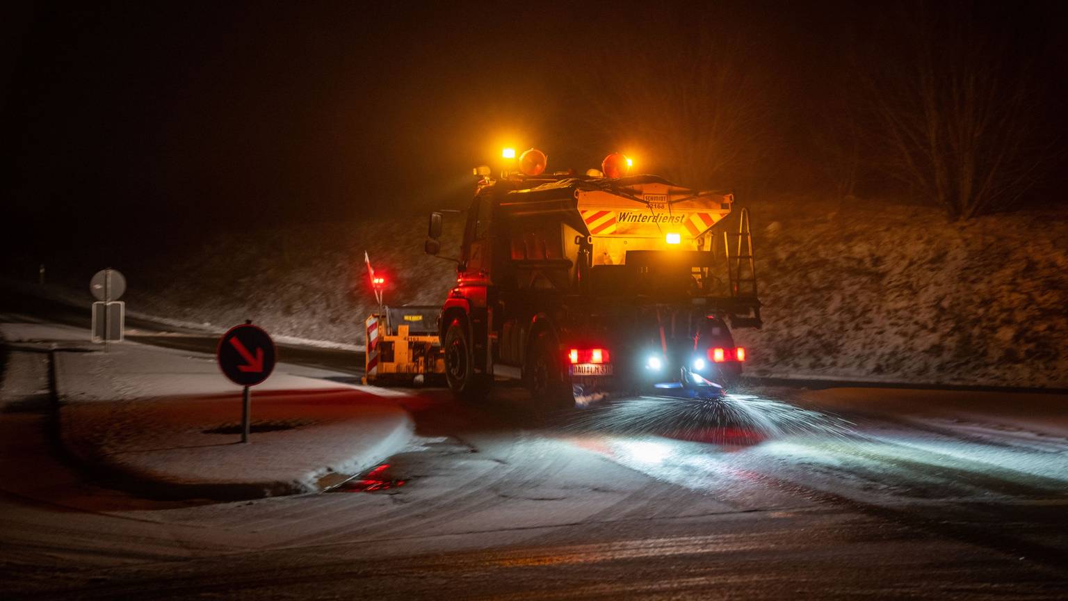 Ein Einsatzfahrzeug des Landesbetrieb Mobilität (LBM) räumt Schnee und streut eine Ausfahrt der B51 gegen Glatteis.