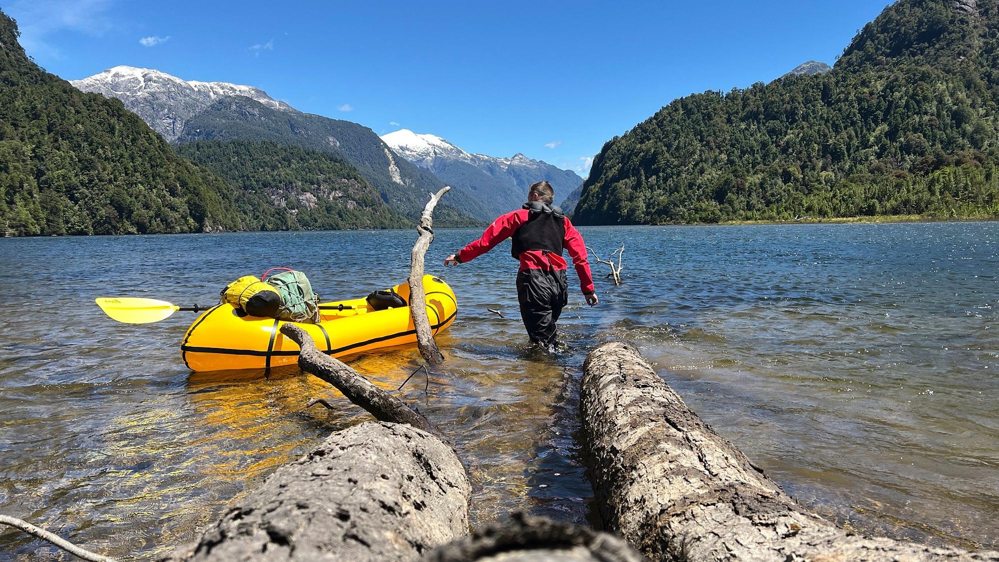 Ein Mann watet durch das Wasser eines Bergsees zu seinem gelben Kajak.