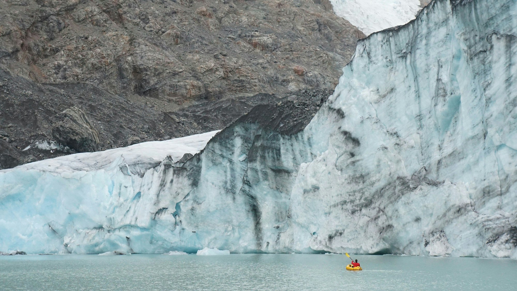 Ein Mann paddelt in einem kleinen Schlauchboot vor einem imposanten Gletscher in Patagonien.